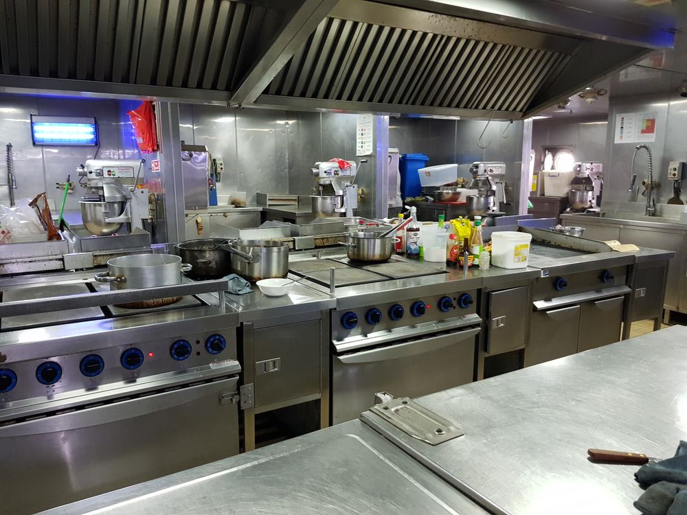 Commercial kitchen with stainless steel appliances, stovetops, and exhaust hood.
