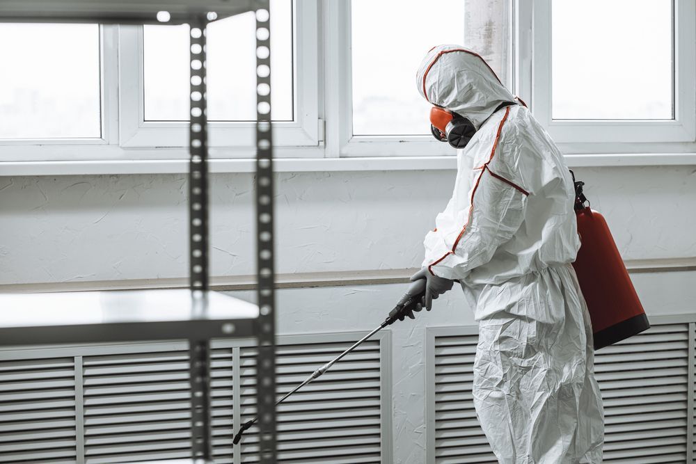 Person in white protective suit spraying insecticide inside a building.