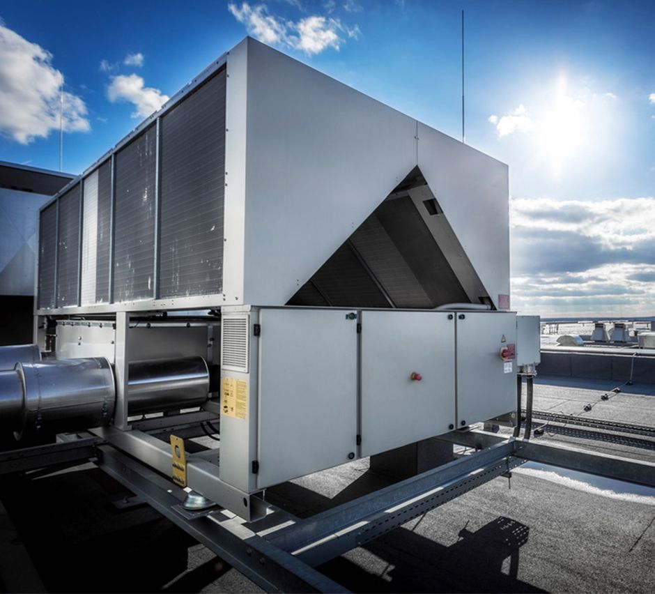 HVAC unit on a rooftop under a bright sunny sky. Metal components and support structure are visible.