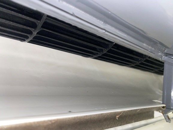 Black vent against a white surface, possibly an air conditioner.