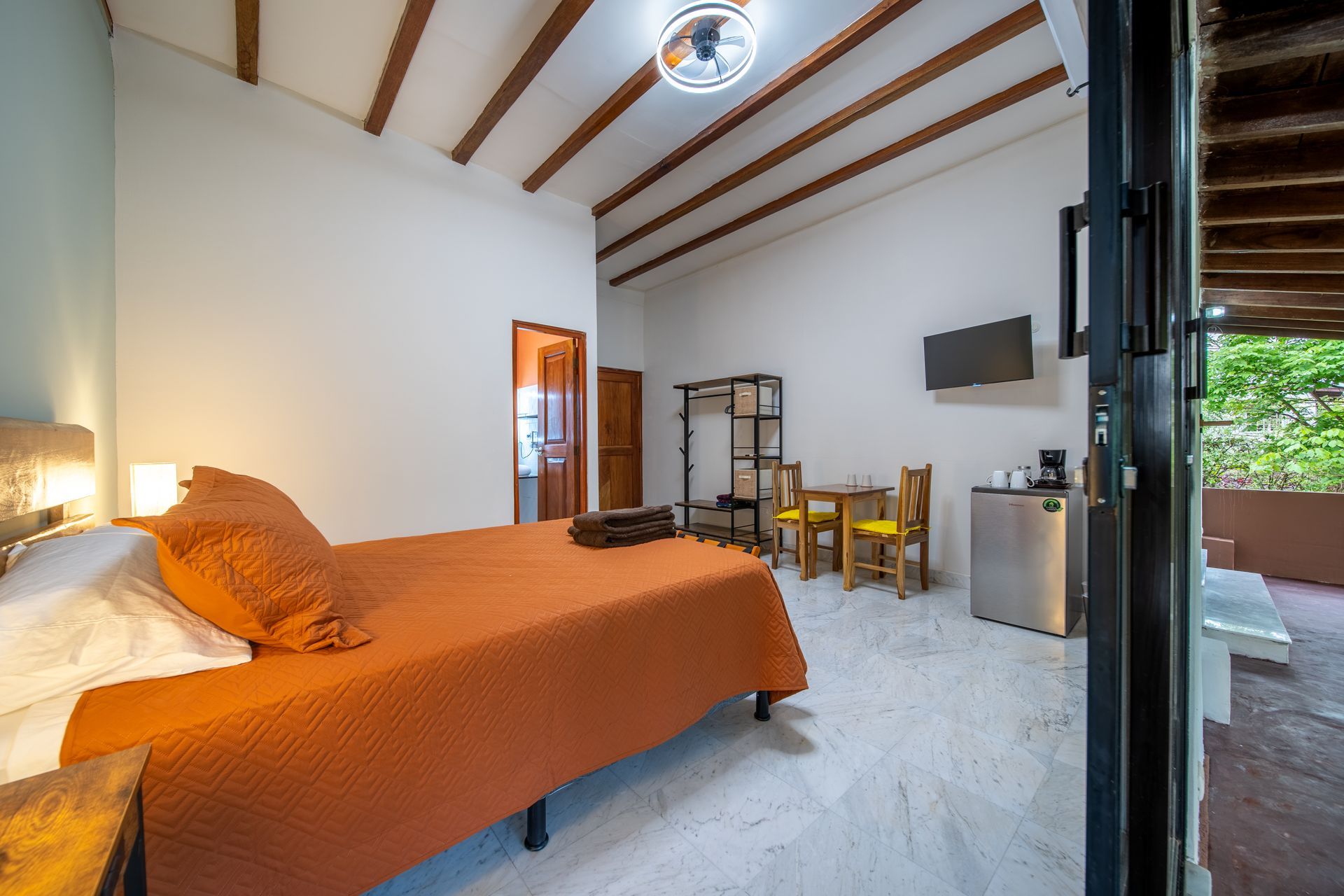 A bedroom with a bed , table , chairs and a refrigerator.