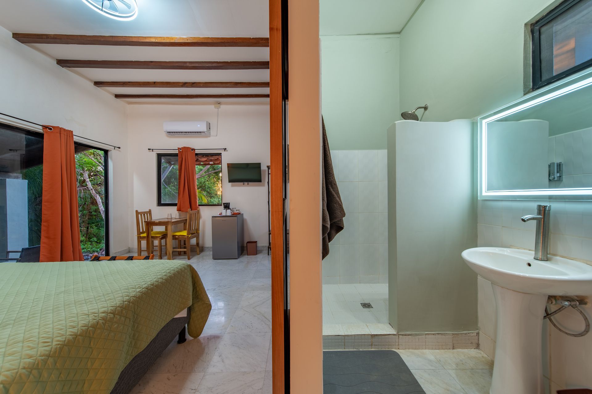A bathroom with a sink and a mirror next to a bedroom.