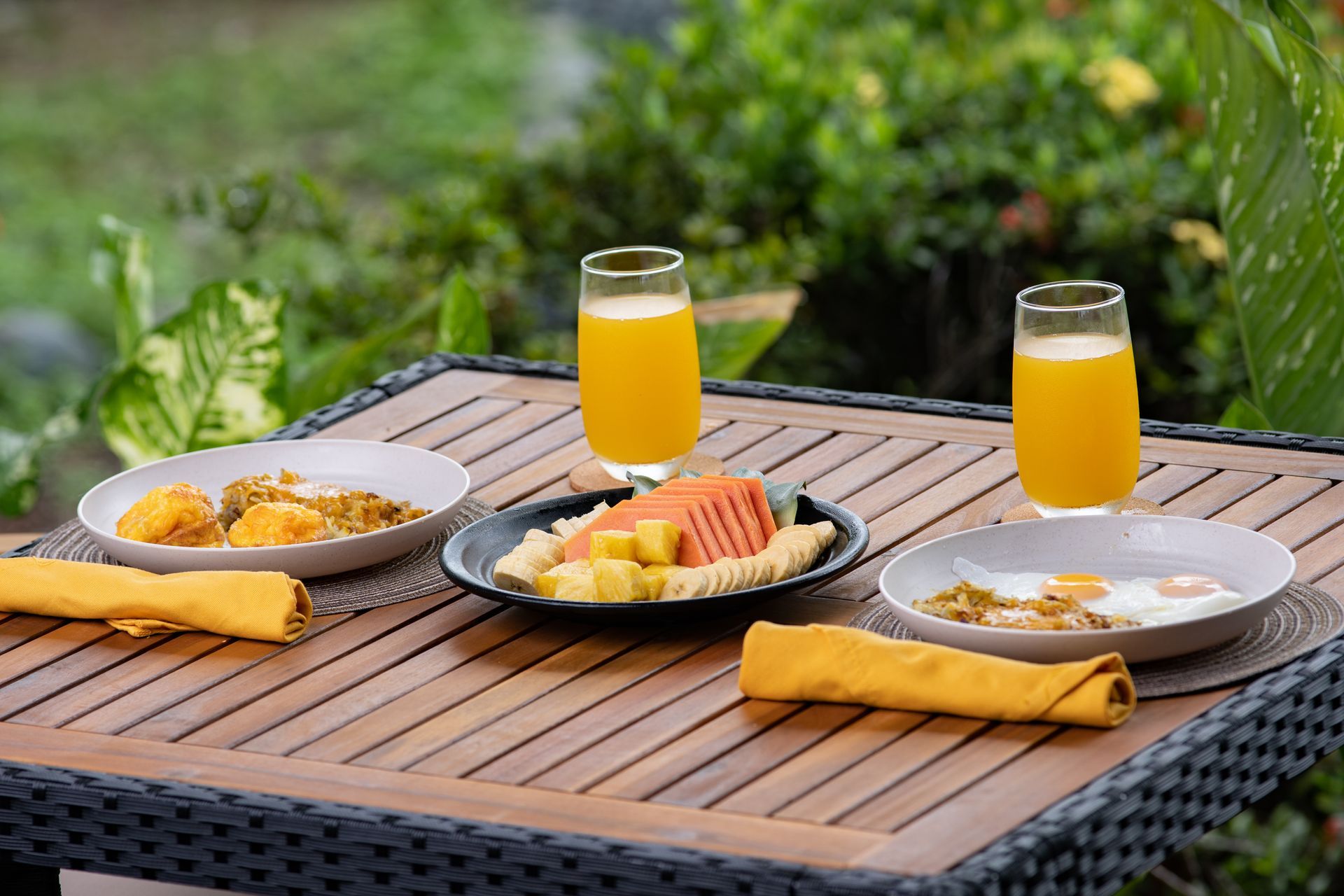 Two plates of food and two glasses of orange juice are on a wooden table.