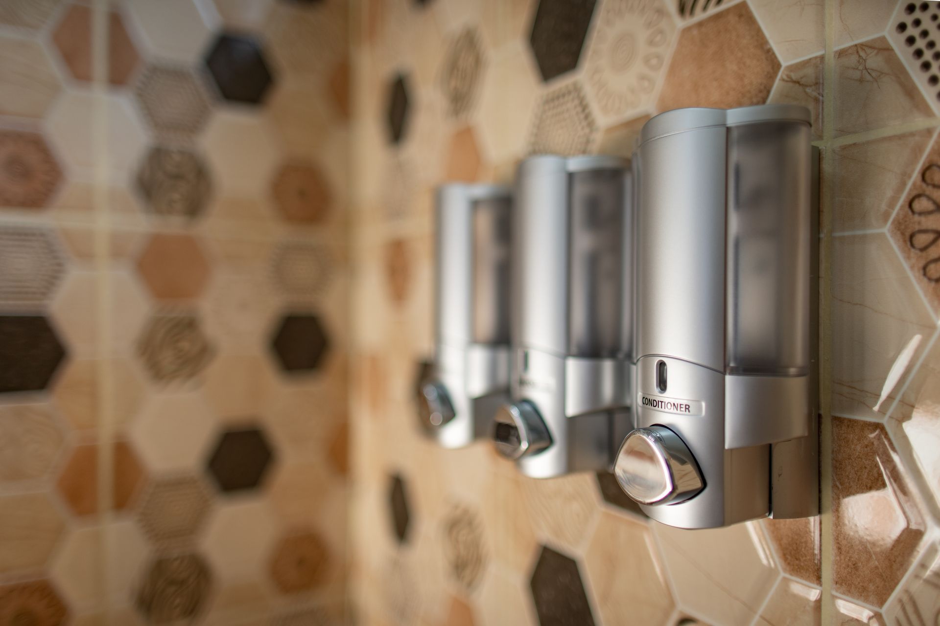 A row of soap dispensers hanging on a tiled wall in a bathroom.