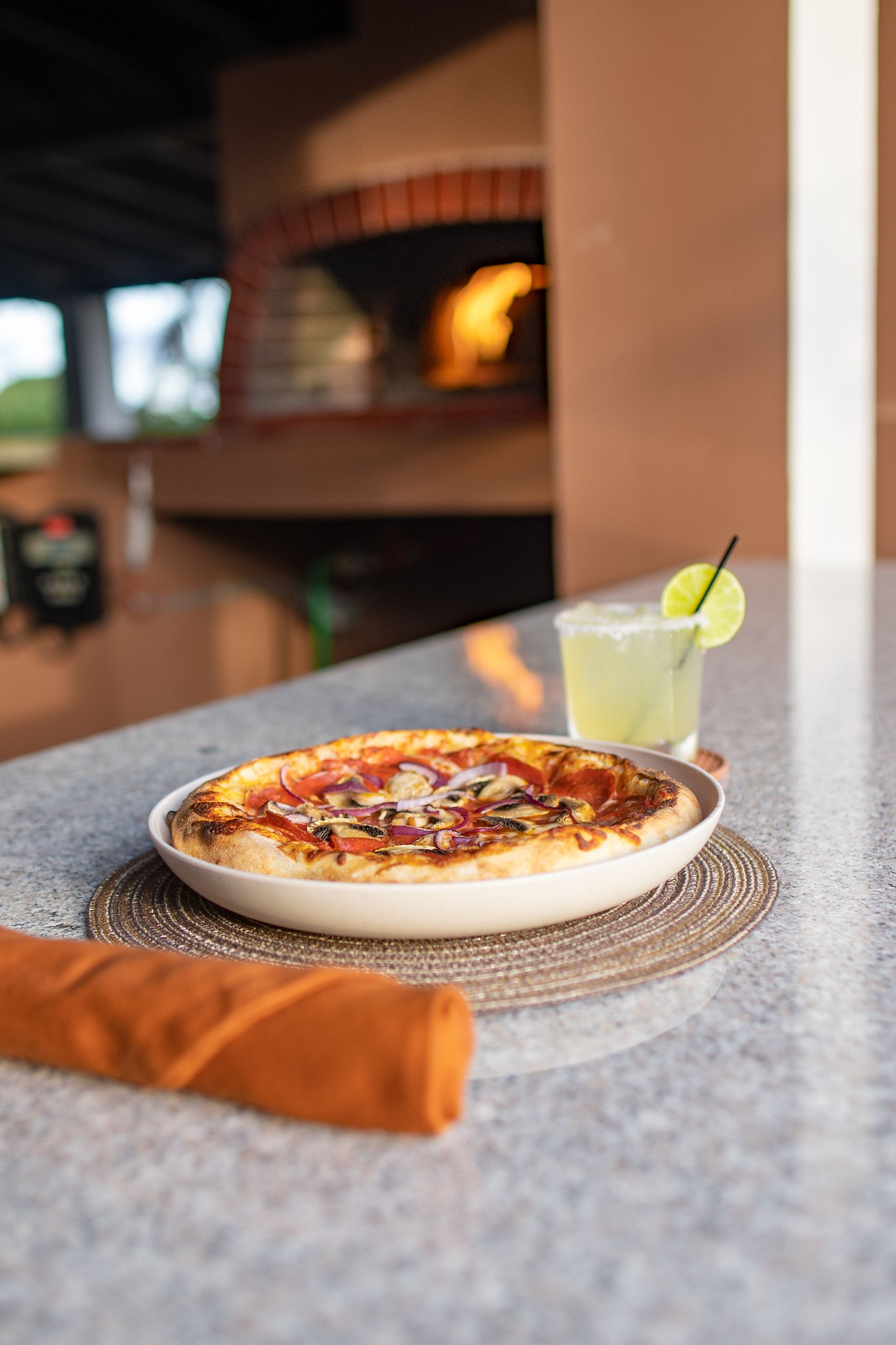 A pizza is sitting on a counter next to a drink.