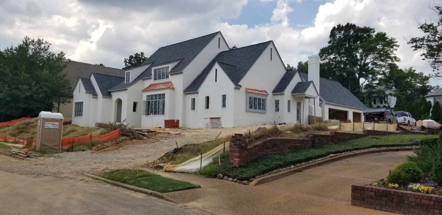 White house under construction with dark roof and gravel driveway.