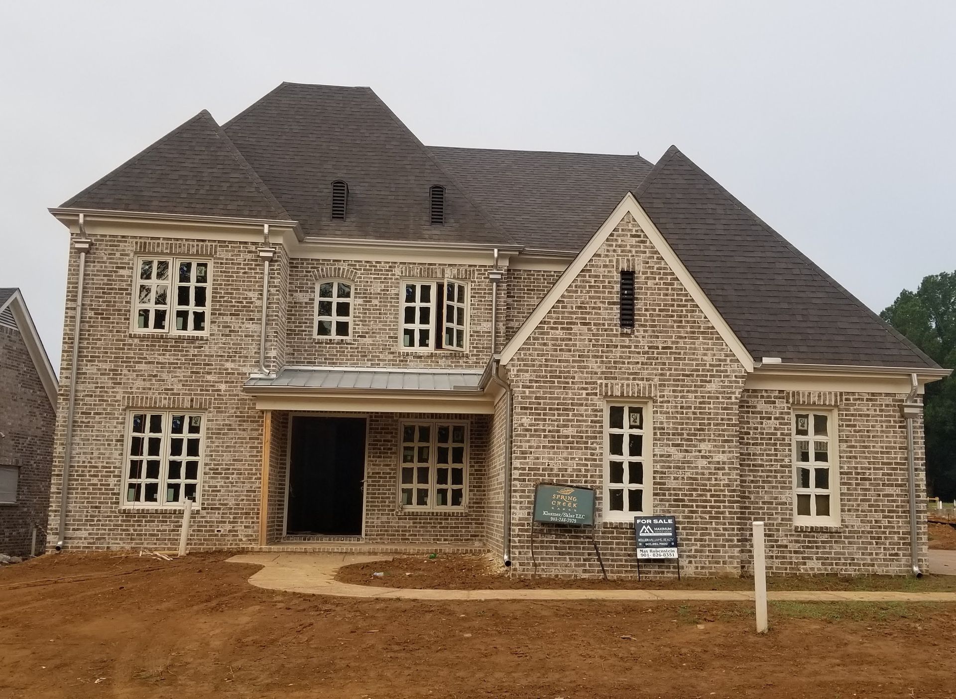 Two-story house under construction with brick facade and dark roof on a brown dirt lot.