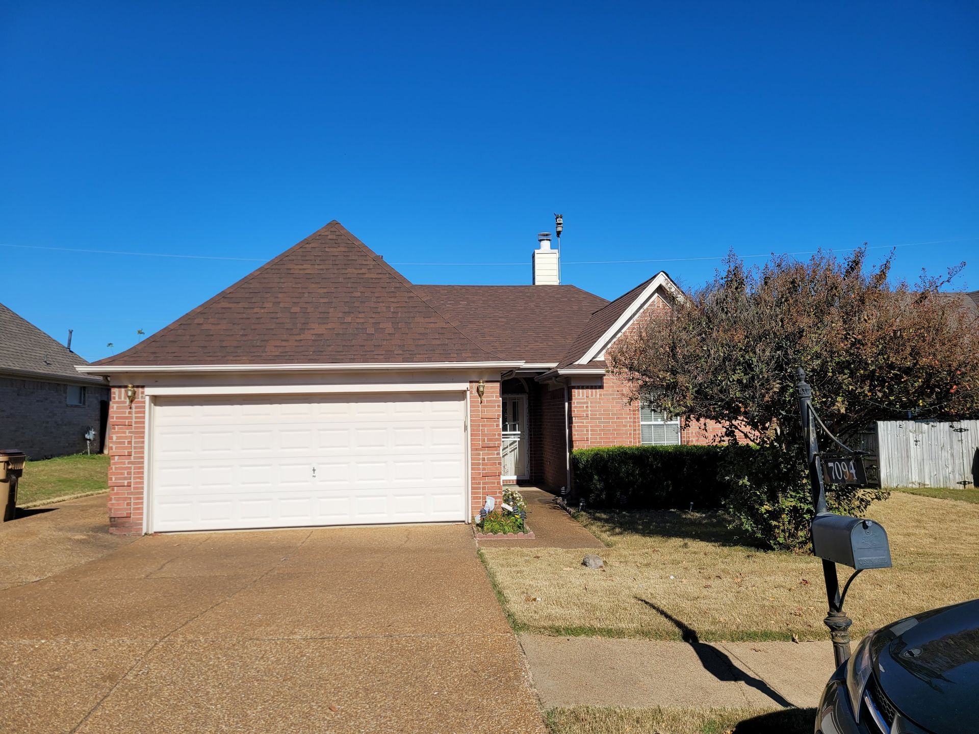 Single-story brick house with brown roof, beige garage door, and clear blue sky.