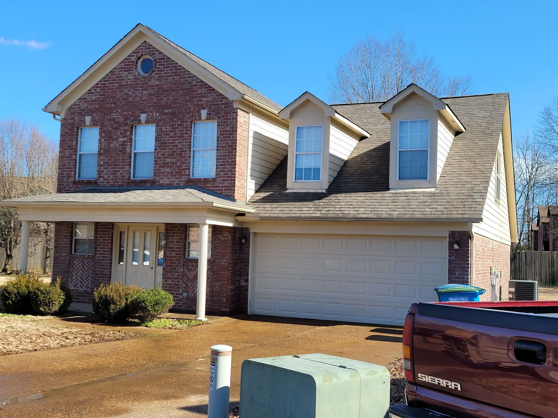 Two-story brick house with beige trim, dormers, and attached garage. A pickup truck is parked in front.