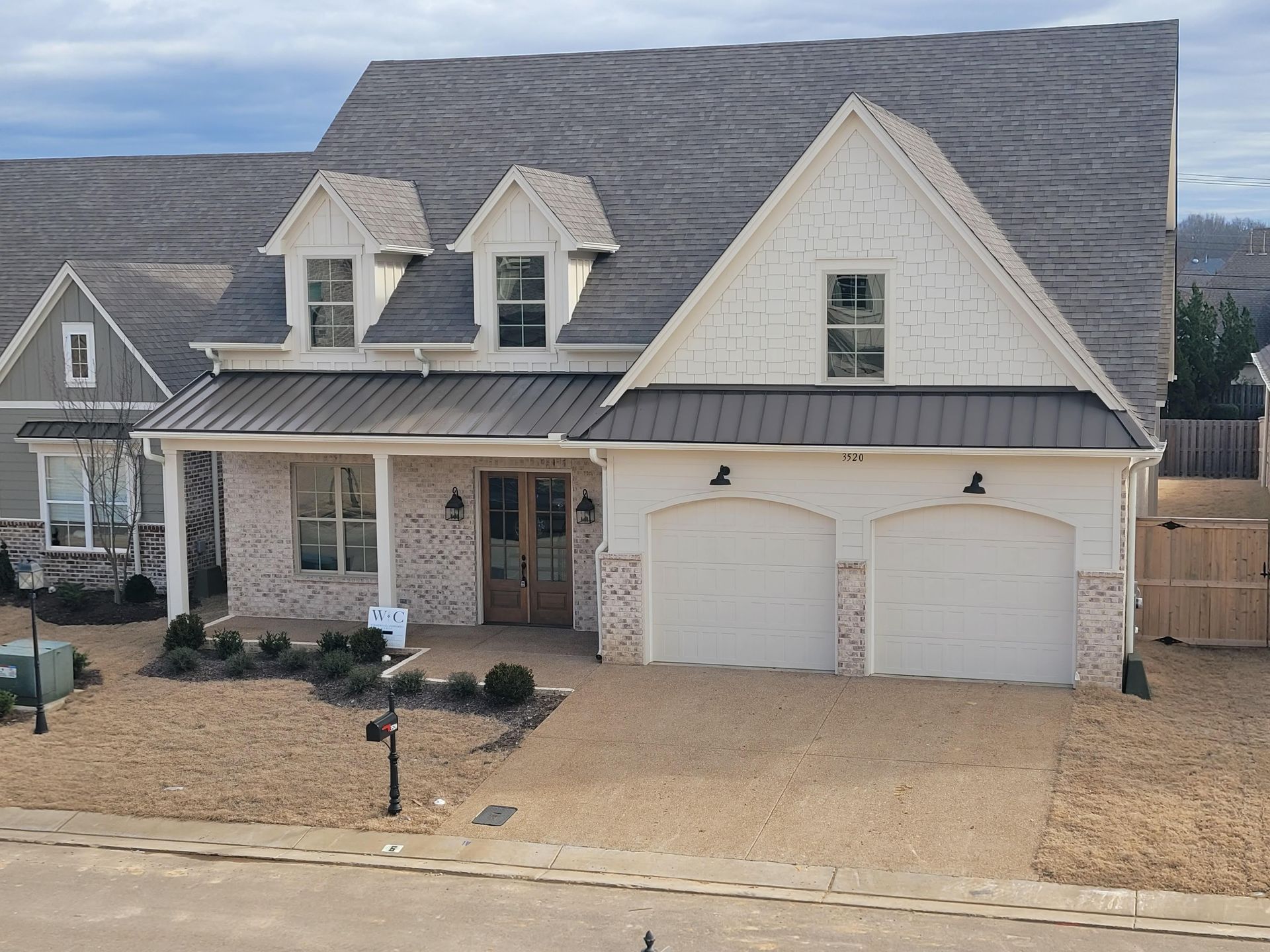 Two-story house with white brick and gray roof. Front porch, two-car garage, and dormers.