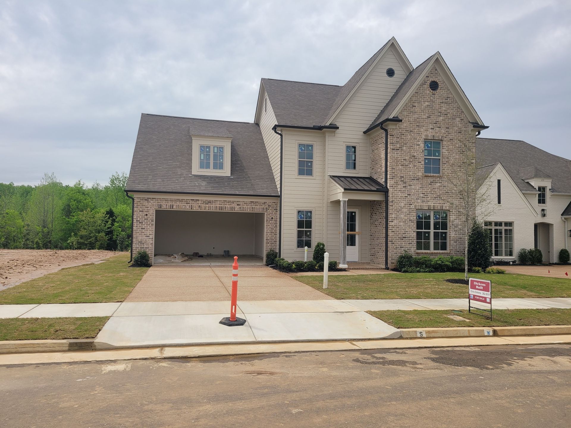 Two-story house with brick and stone facade, unfinished garage, and a driveway under a cloudy sky.