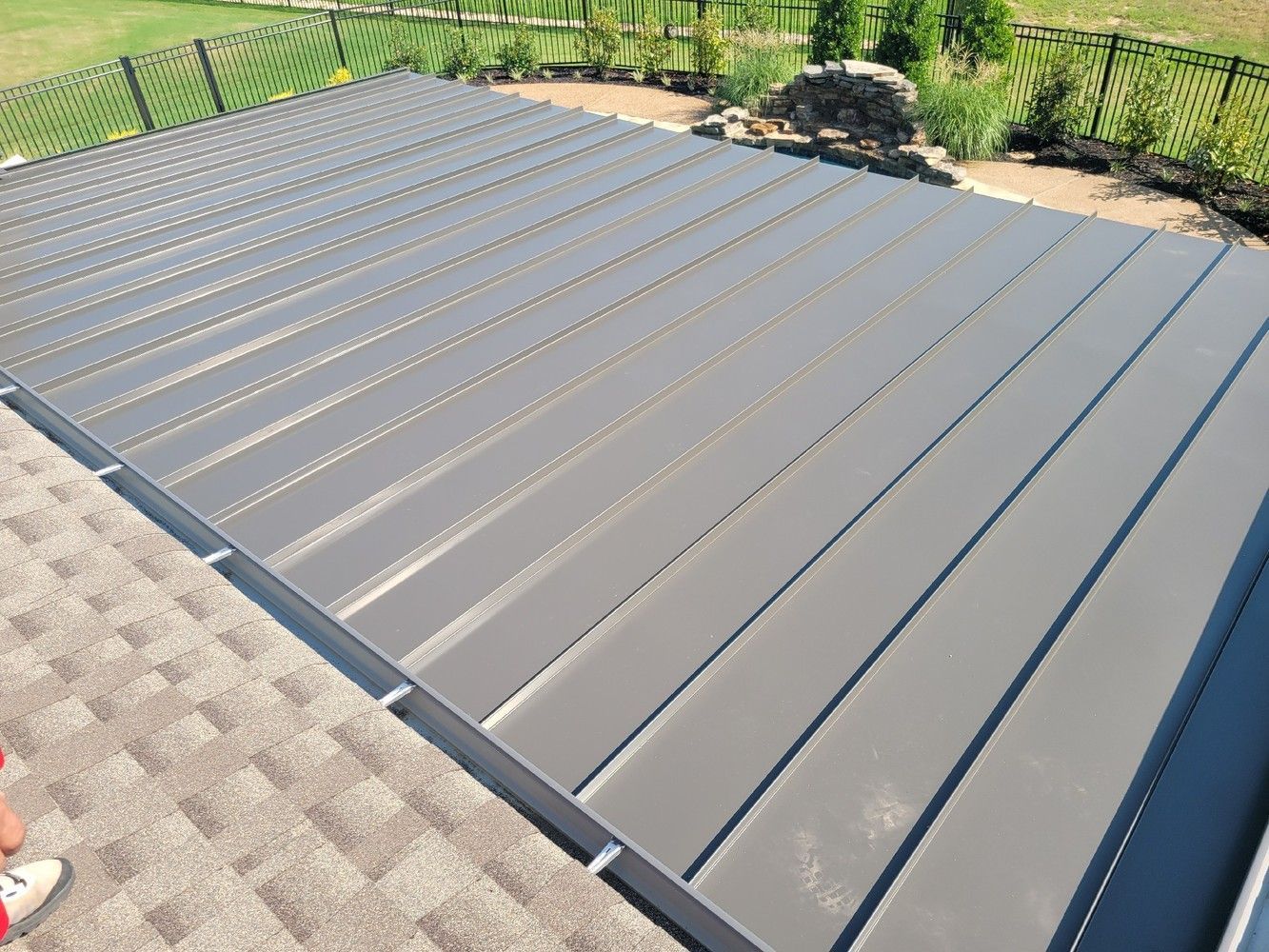 Gray metal roofing on a house with a grassy backyard and a gravel-covered roof section.
