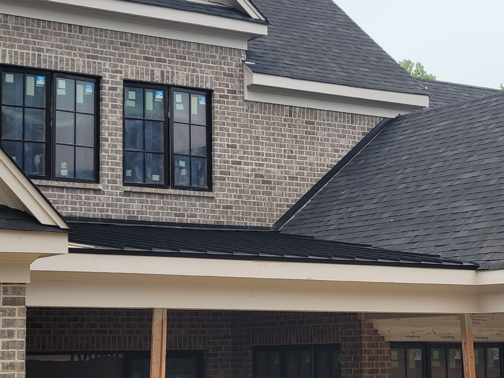 Brick house with dark windows and roof under construction.