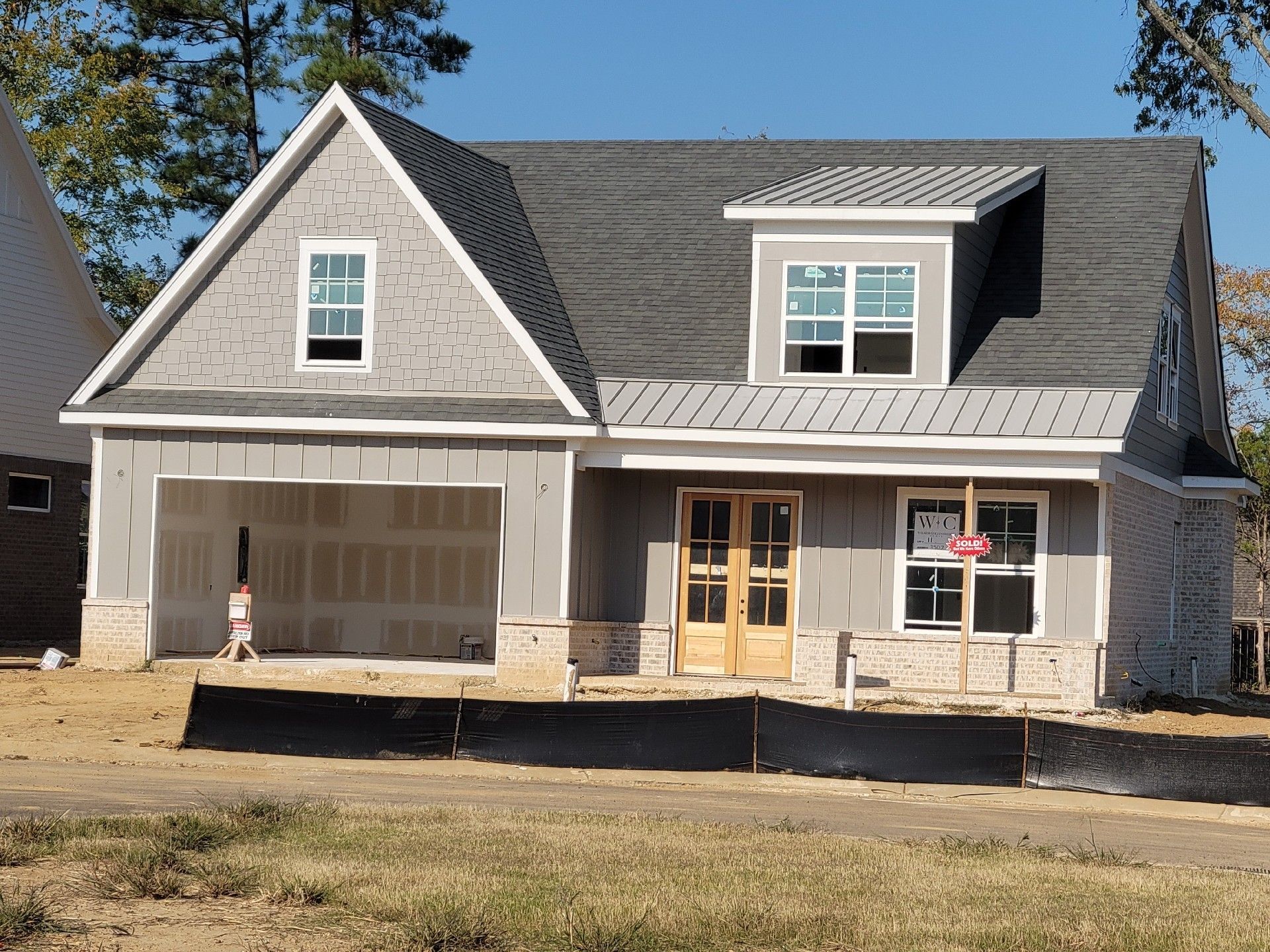New house under construction, gray siding, garage, front door, windows, brick accents.