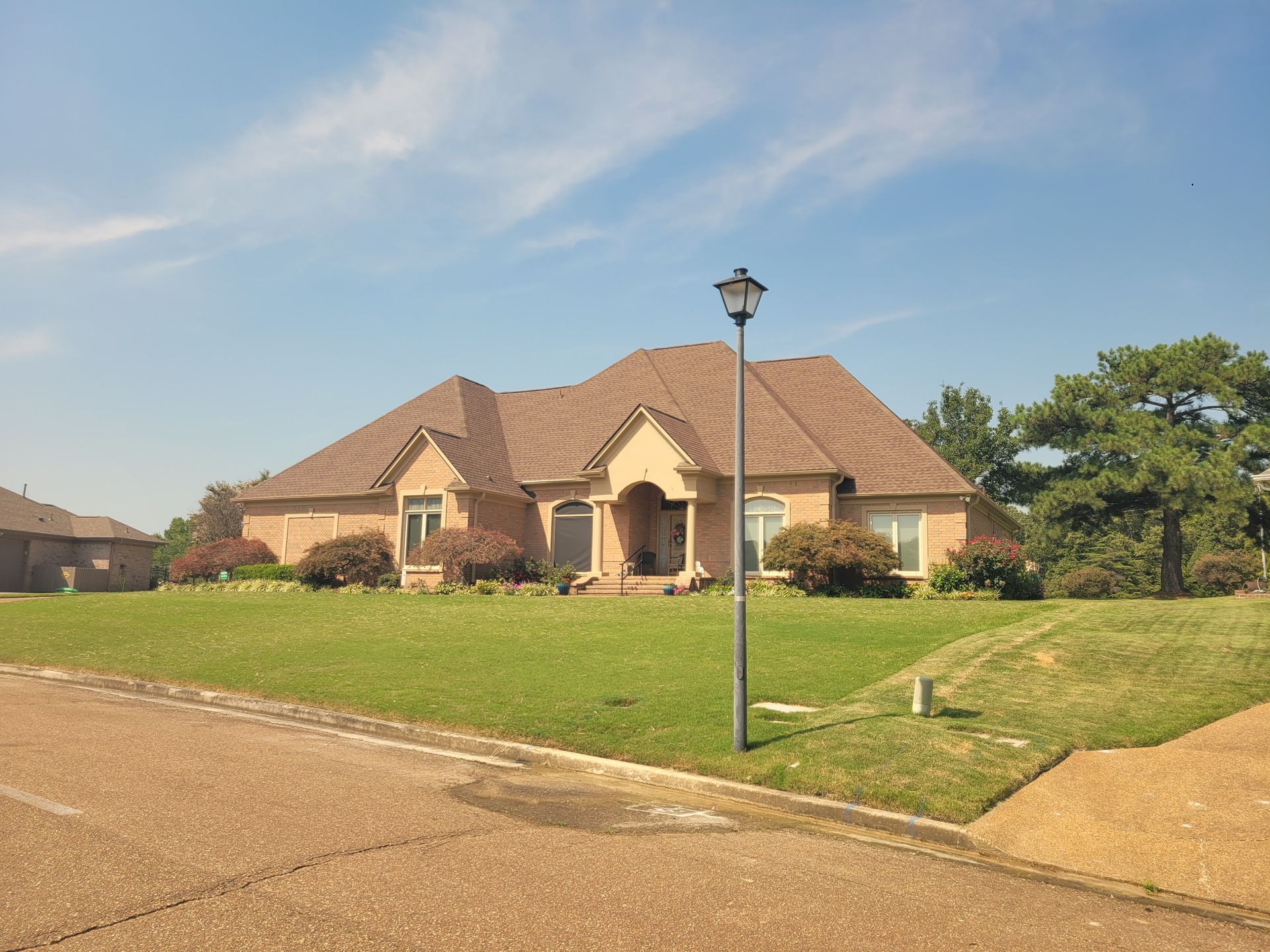 Brick house with brown roof and green lawn under a blue sky.