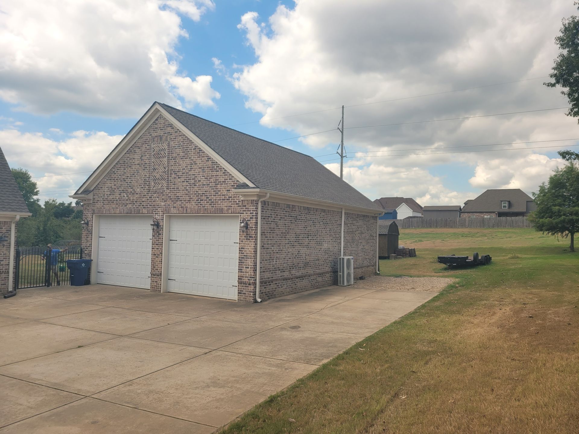 Two-car brick garage with white doors on a concrete driveway, green lawn under a cloudy sky.