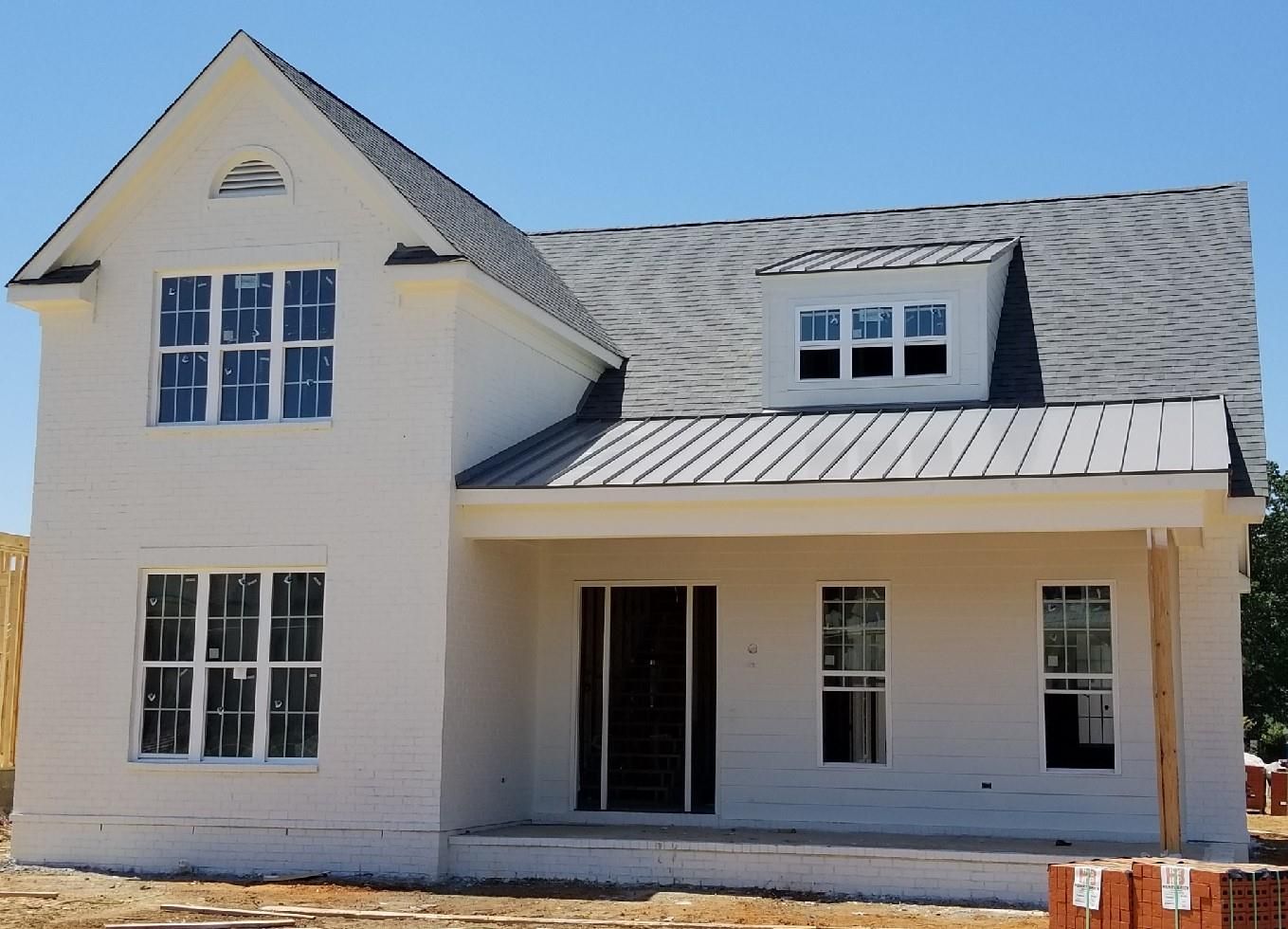 White two-story house with a gray roof under a blue sky; construction site.