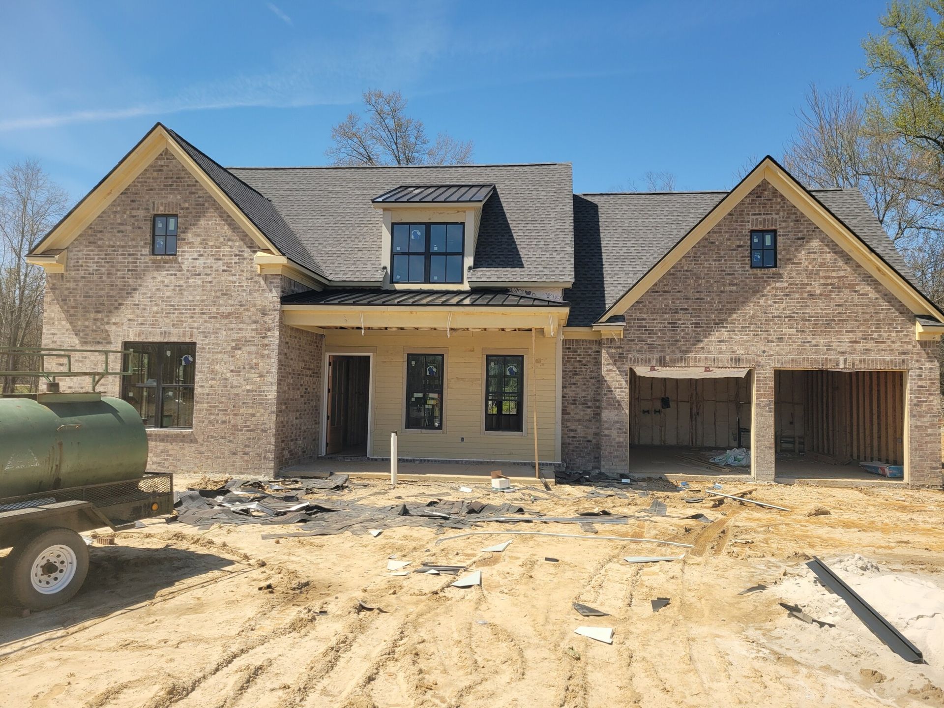 New brick house under construction with a dark gray roof and exposed wood.