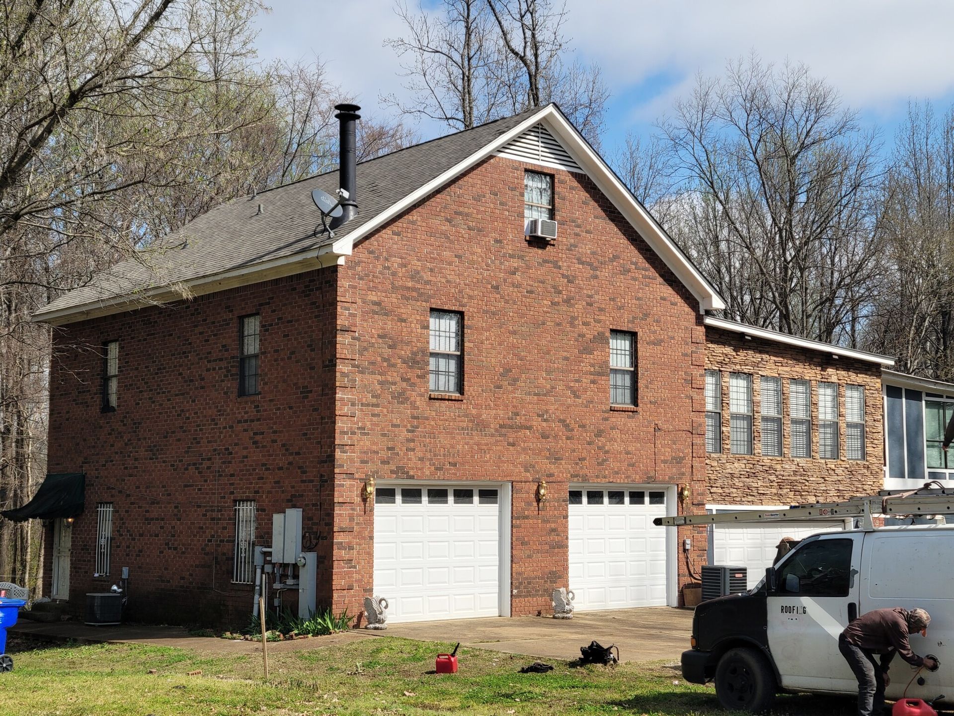 Brick building with two garage doors, windows, and a parked van. A person works near the van.