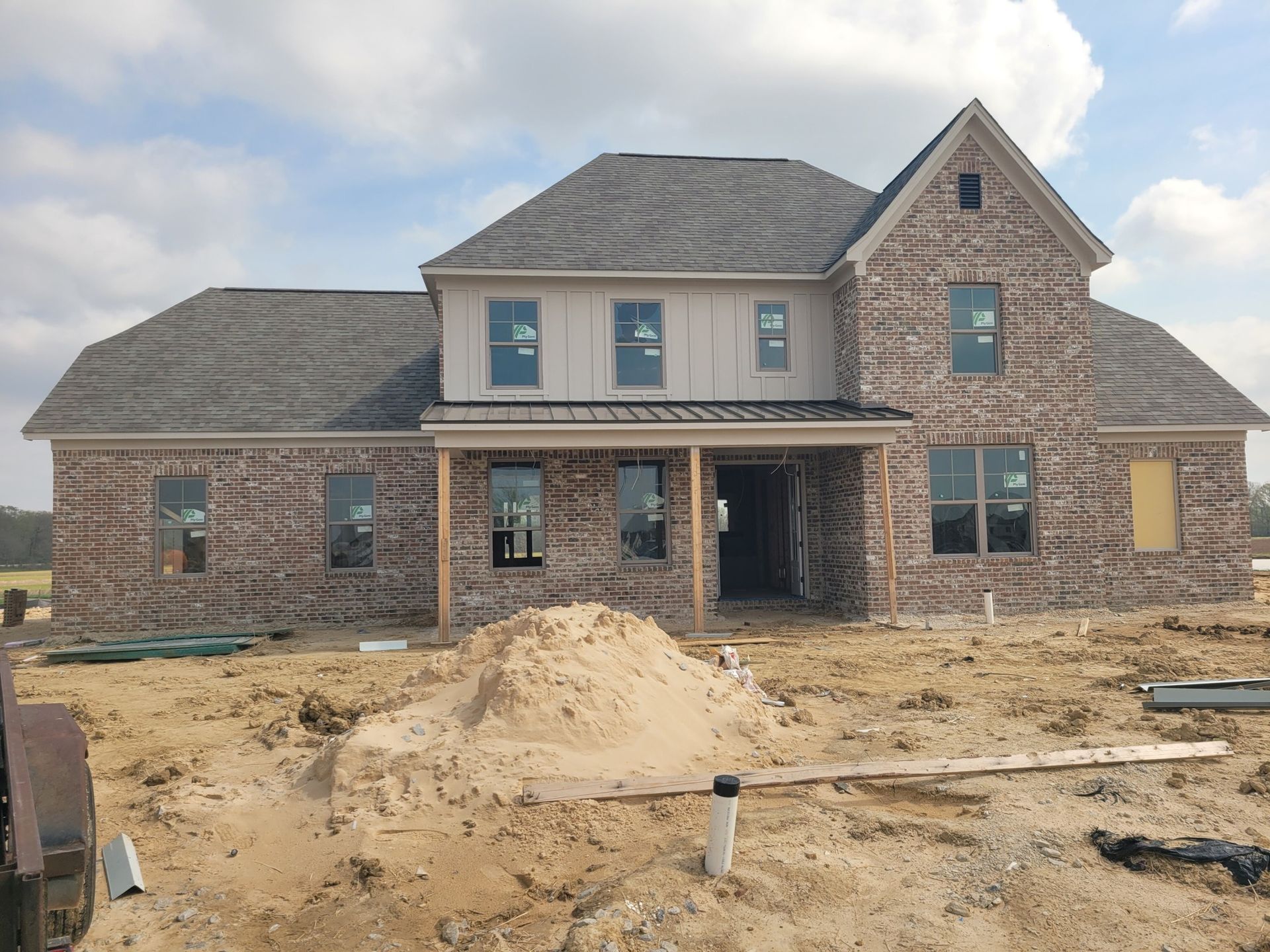Two-story brick house under construction; windows, siding, and a porch.
