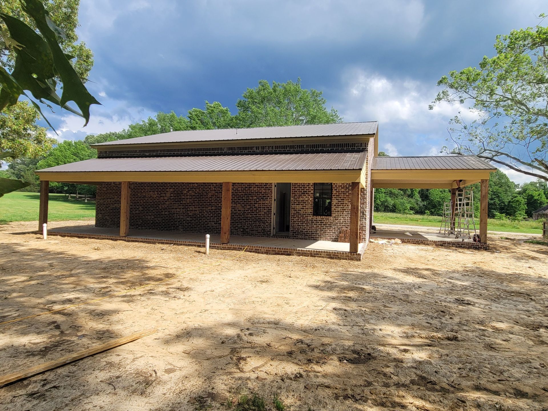 A partially built rectangular structure with a metal roof, brick walls, and a covered porch. Set outdoors.