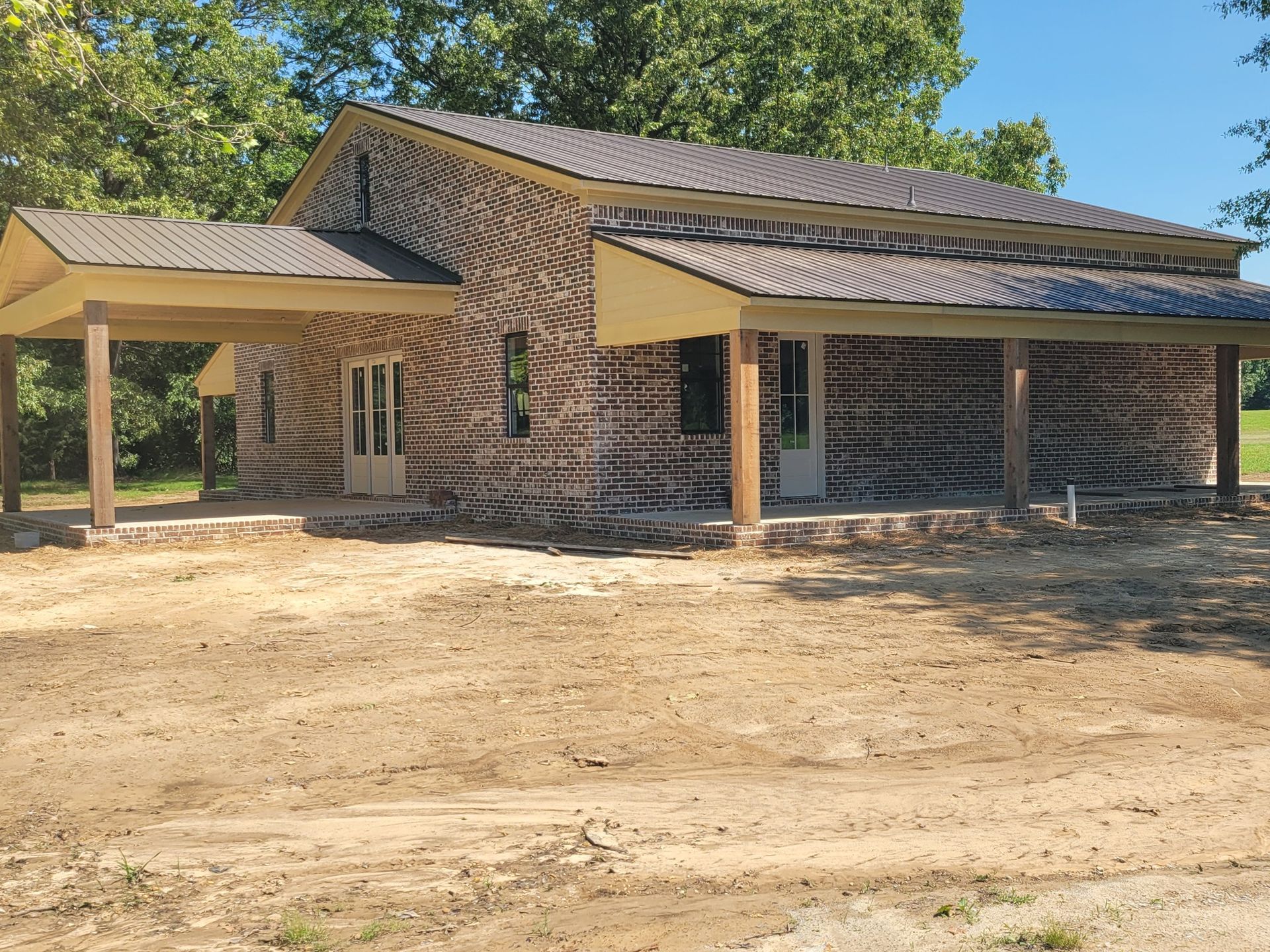 Brick house with covered porch and carport in a dirt yard. Brown roof and wooden posts.