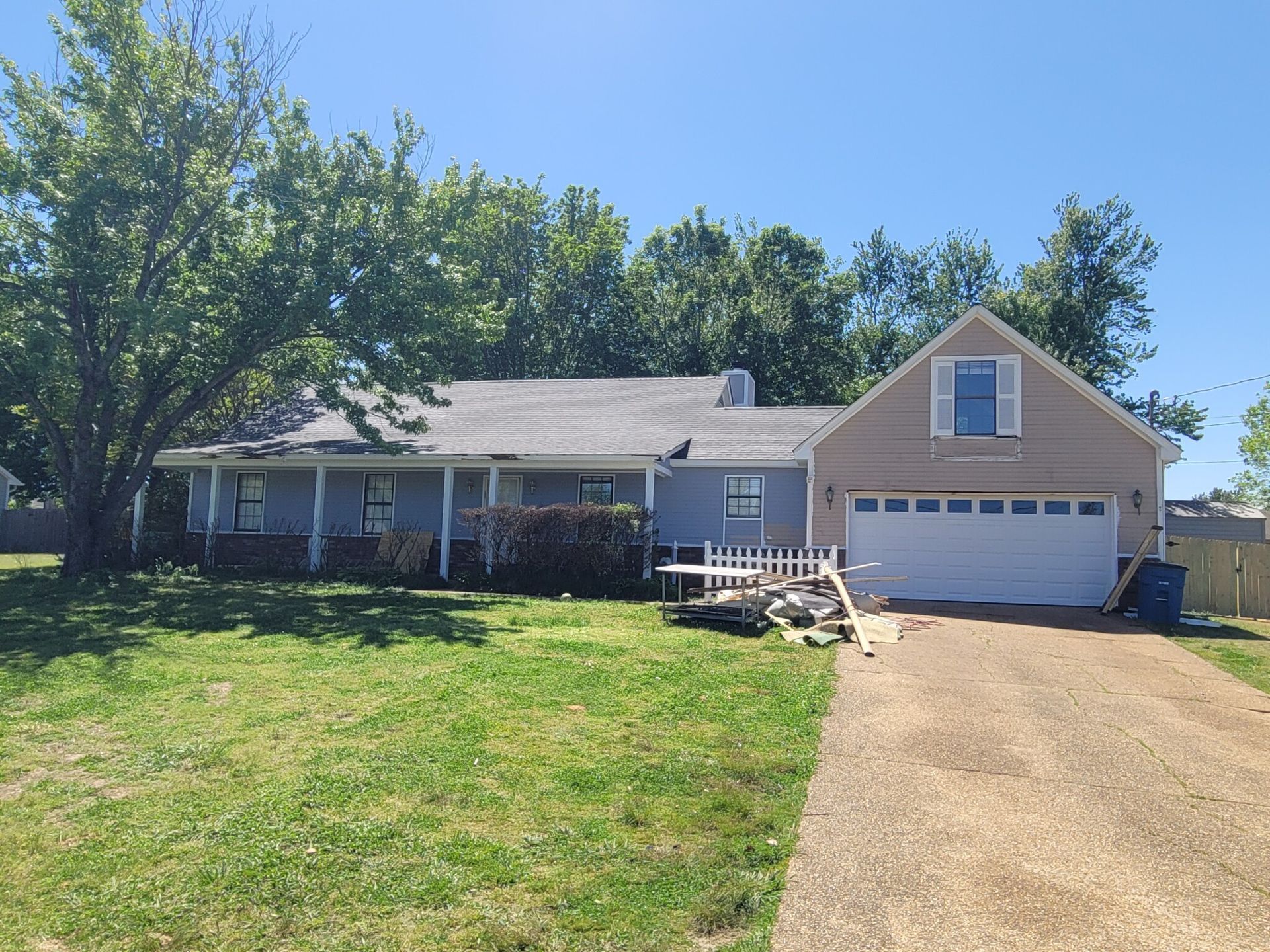 House with gray siding, white garage door, porch, and long driveway on a grassy lawn.