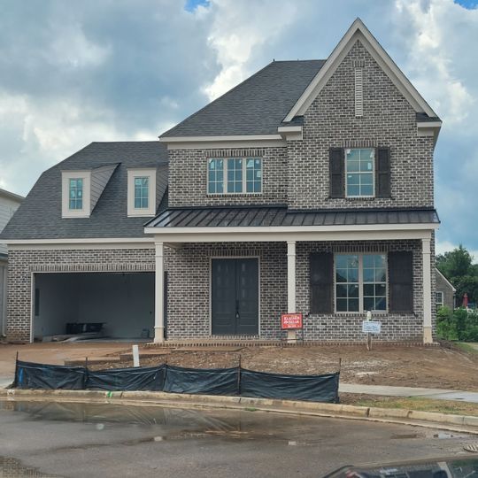 New brick two-story house under construction with black shutters and a gray roof, cloudy sky.
