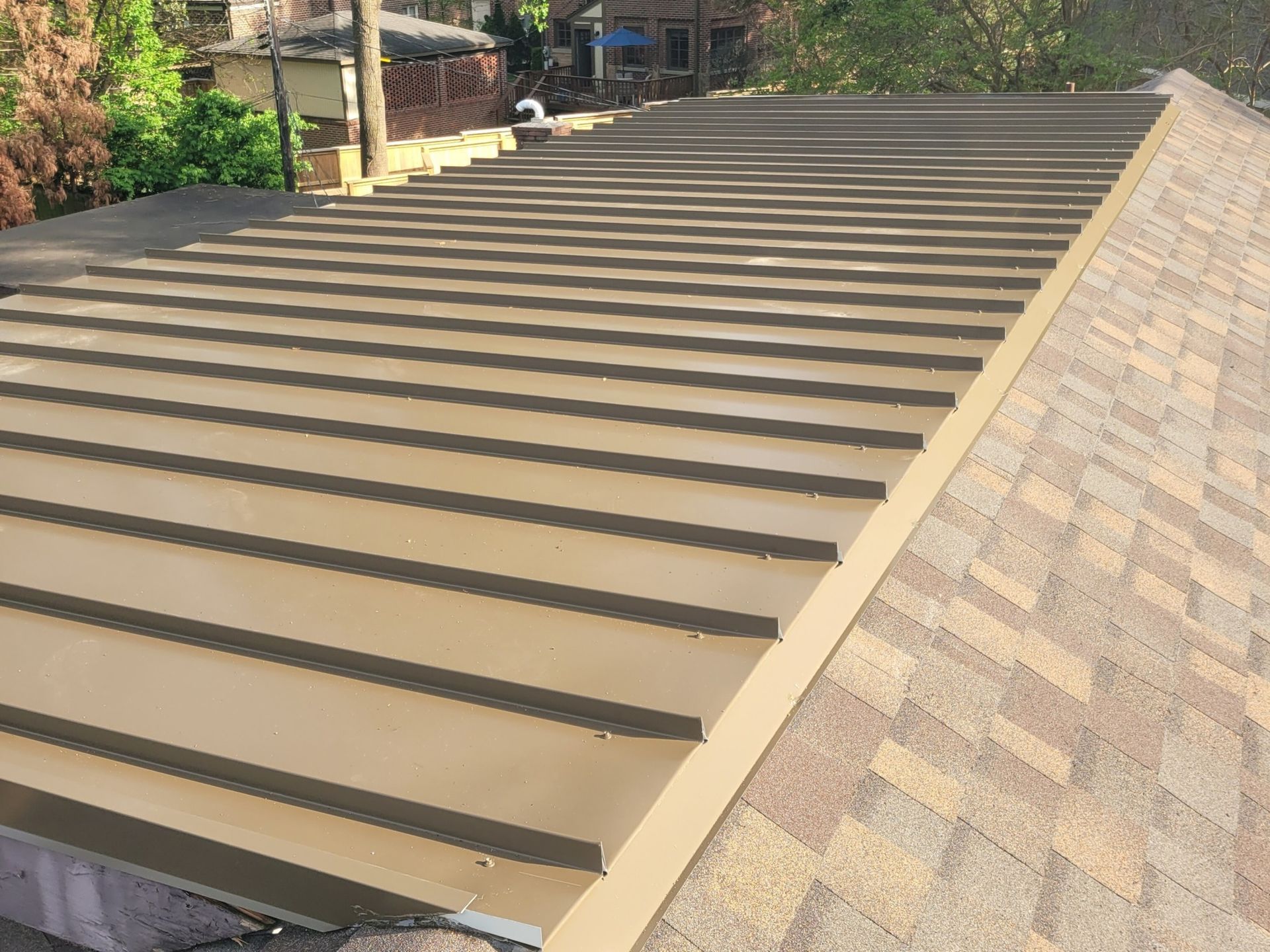 Tan metal roof next to a brown shingle roof, outdoors.