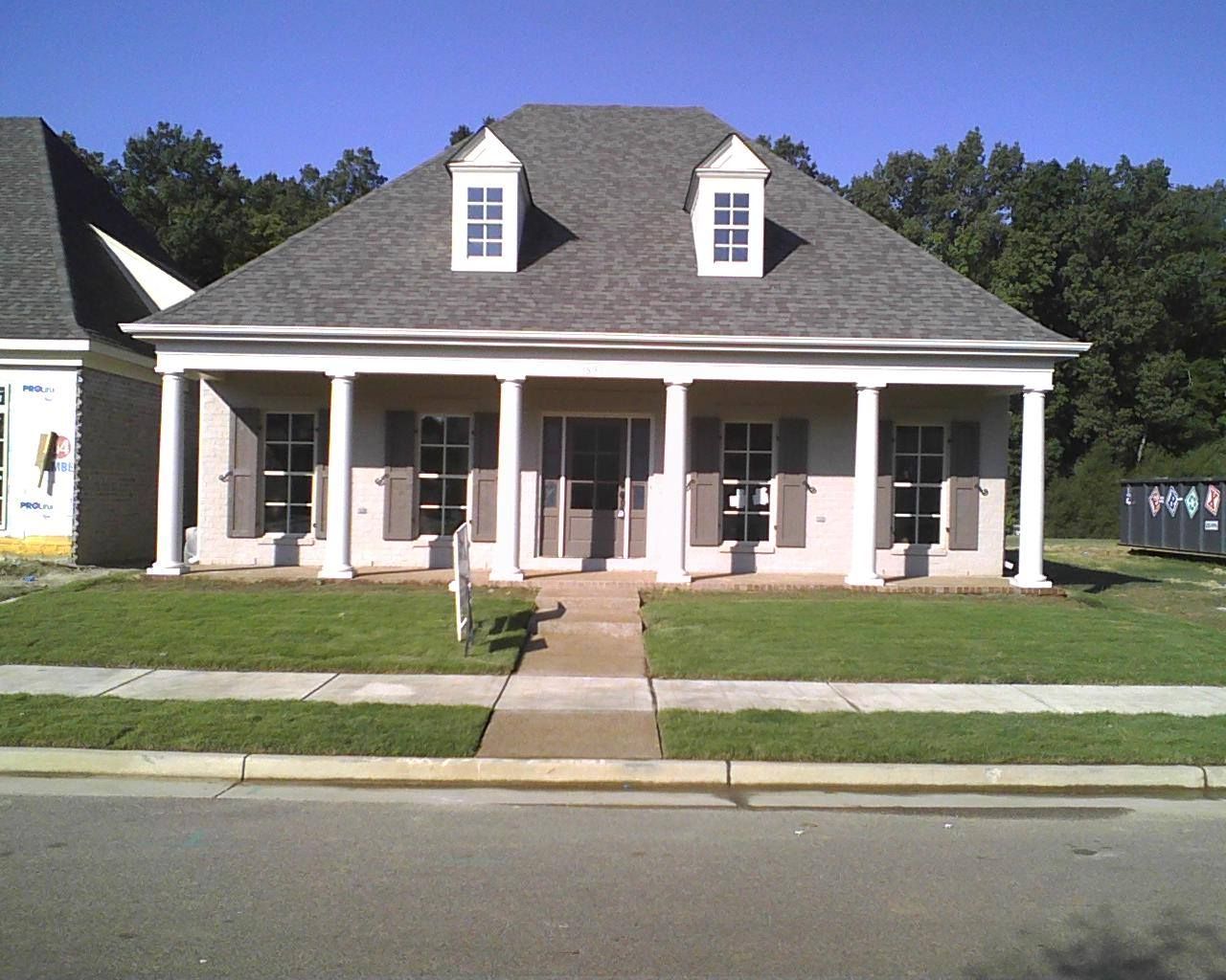 House with white columns, shutters, and a gray roof. Green lawn and sidewalk in front.