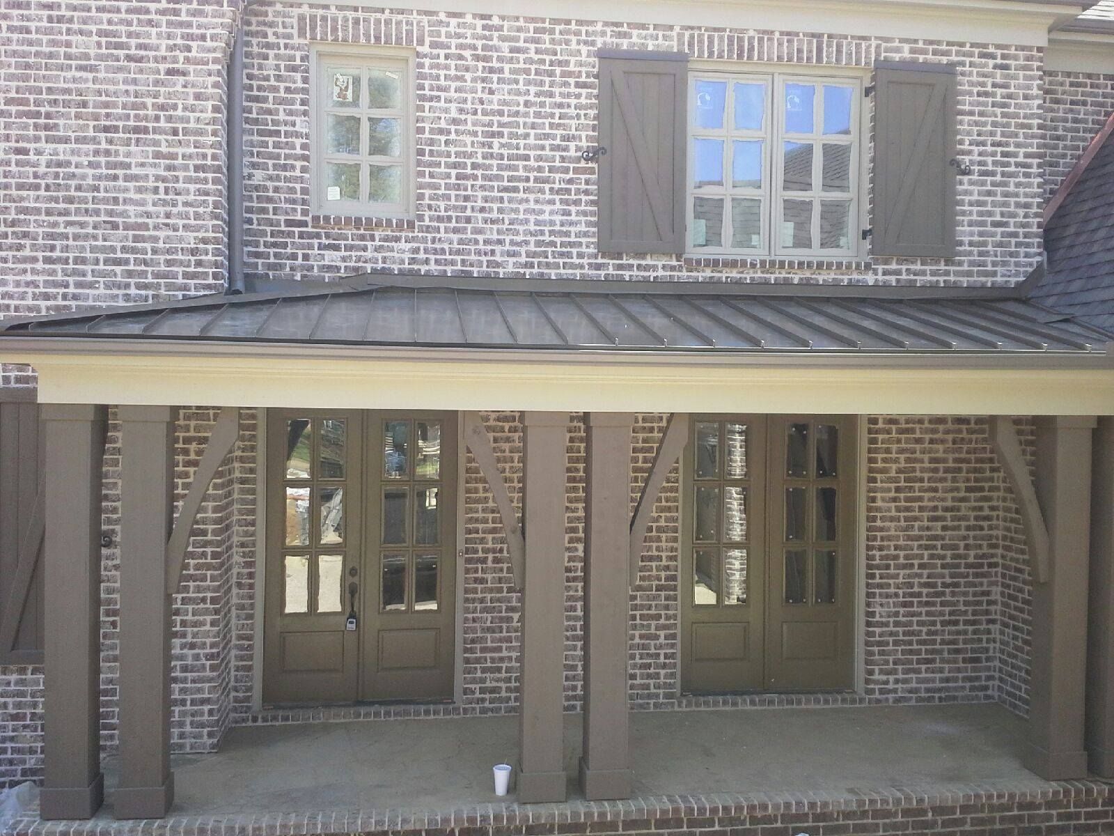 Brick house exterior with brown shutters, door, and columns, covered porch.