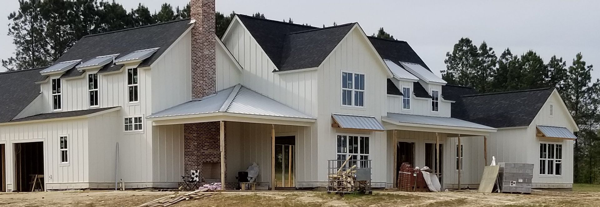 White farmhouse under construction with dark roof and chimney.