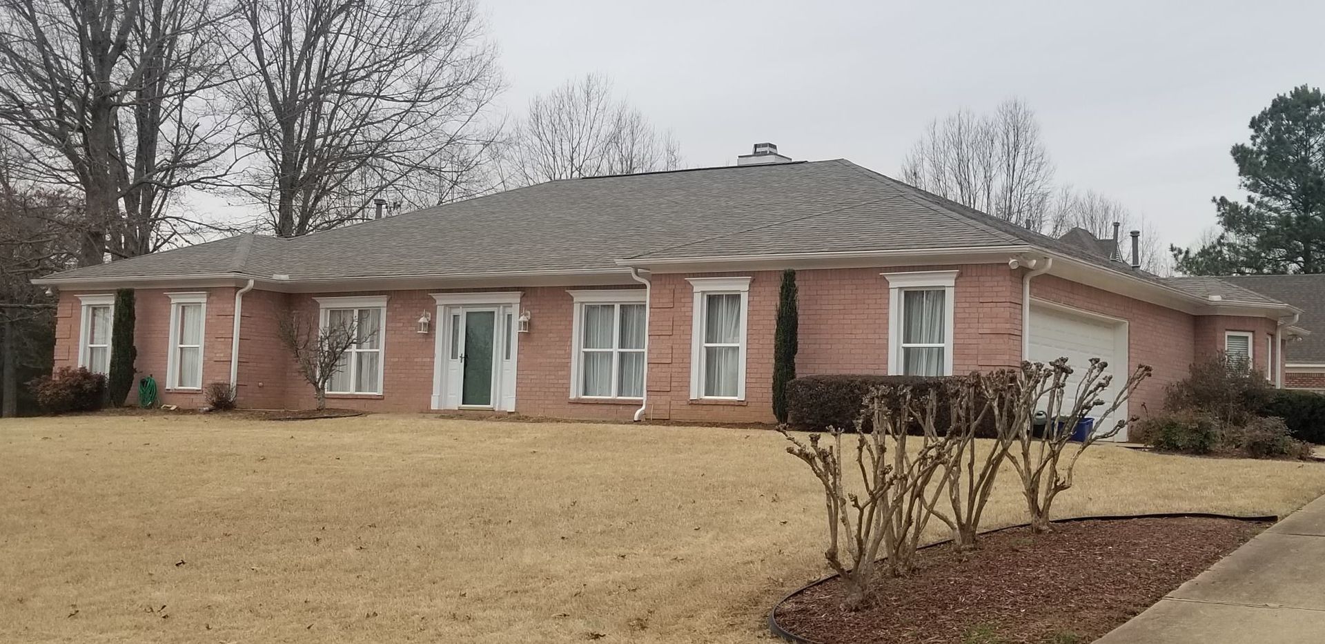 Brick house with a brown roof, windows with white frames, and a brown lawn.