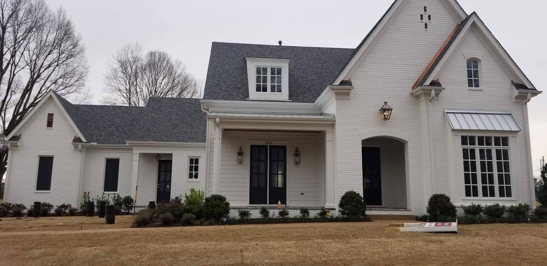 White brick house with black roof, windows, and door frames. Brown grass in the foreground.