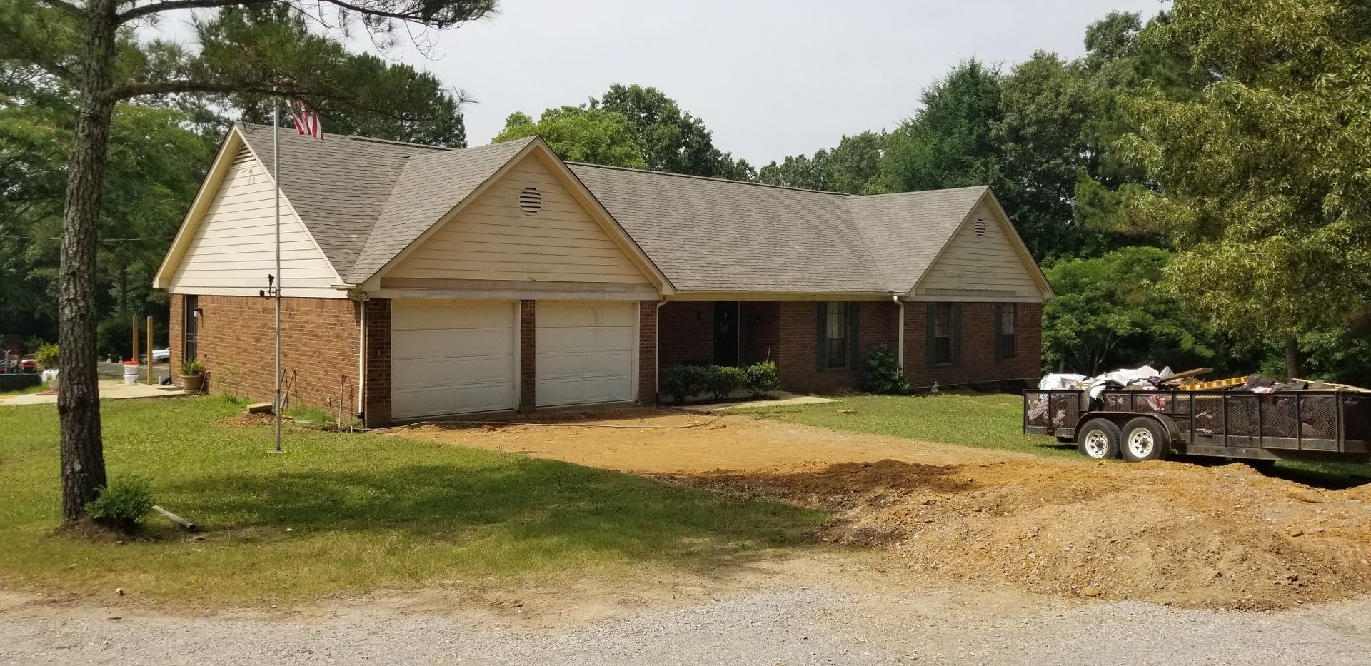 A house with a brick facade and two-car garage; a trailer sits in front of the house.