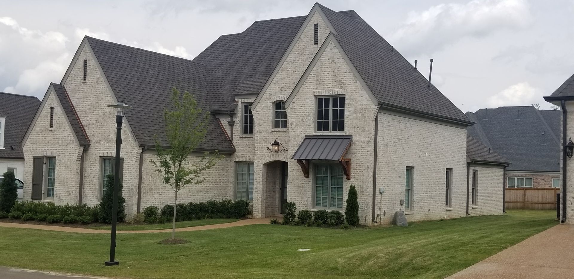 Large, light-colored brick house with a dark gray roof and a small patch of green grass in front of it.