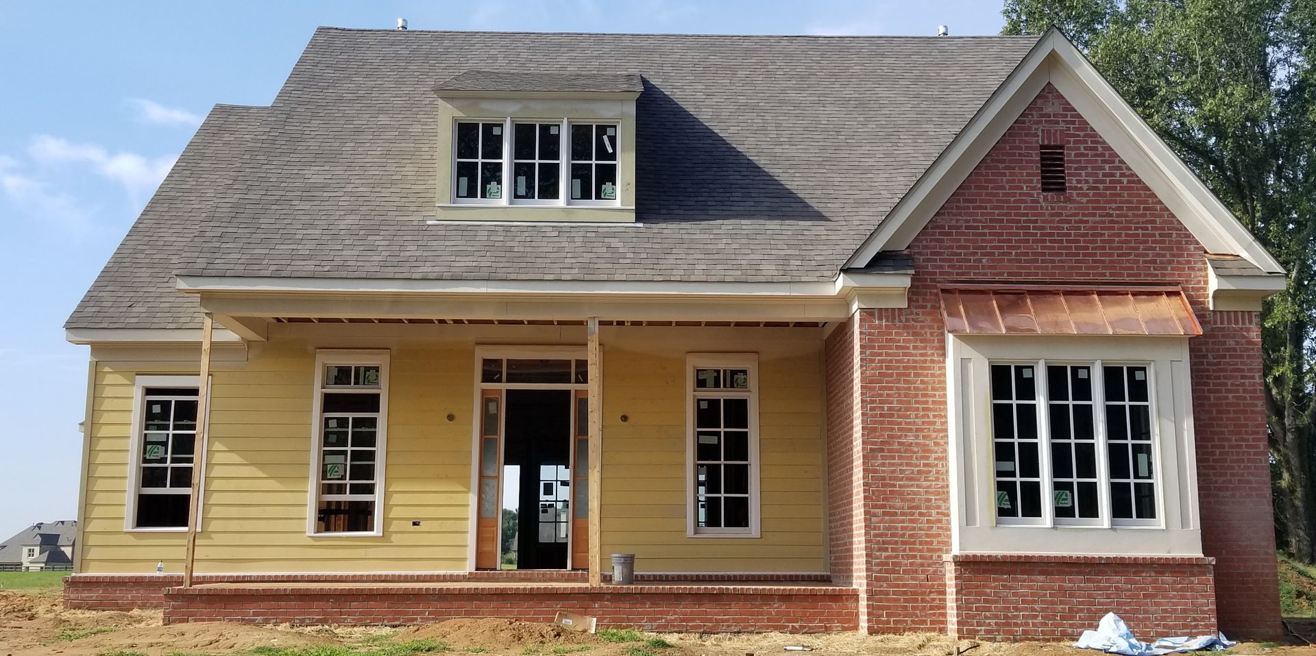 New house under construction; yellow siding, red brick, gray roof, white windows and trim, blue sky.