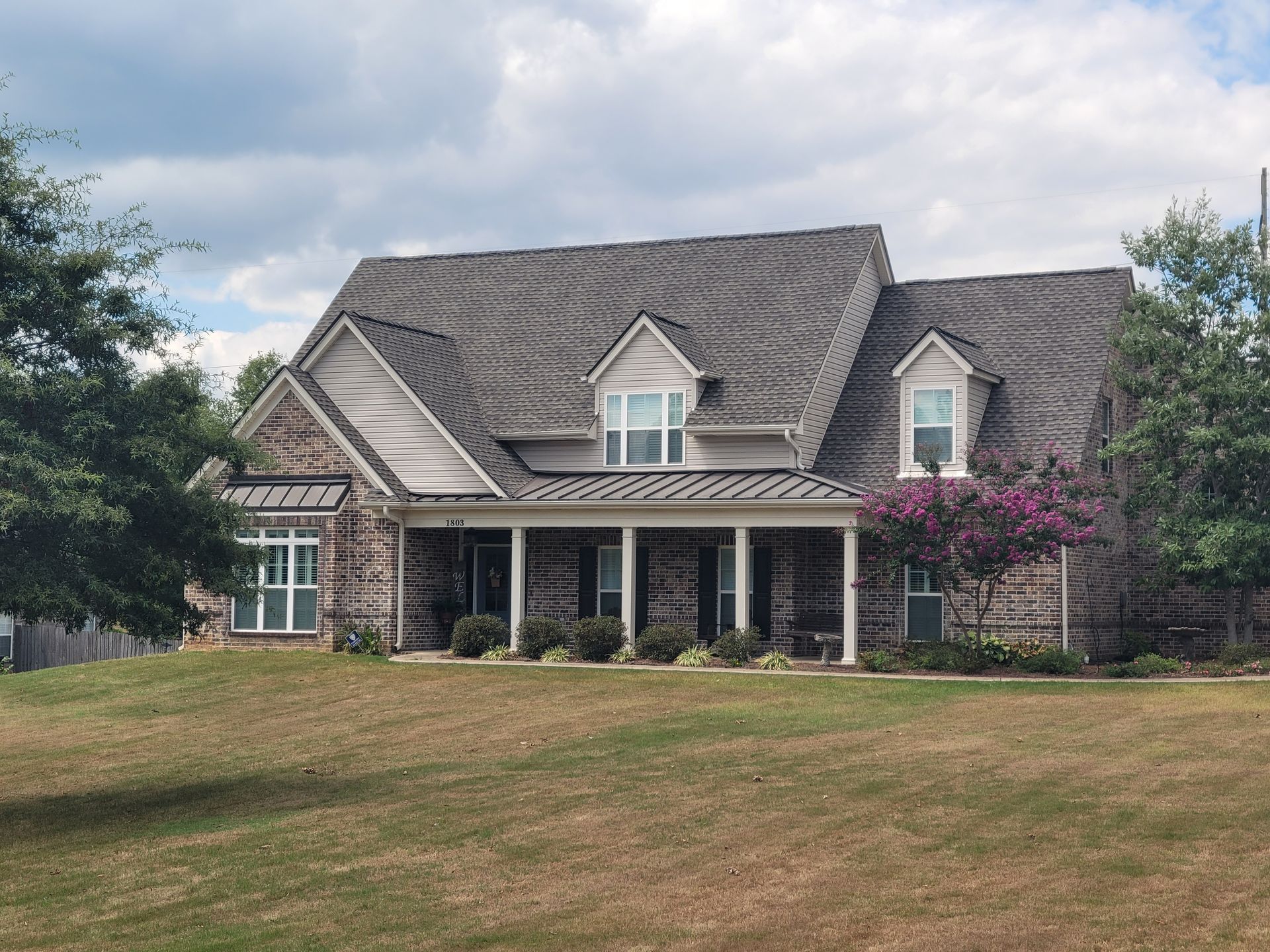House with gray siding, white garage door, porch, and long driveway on a grassy lawn.