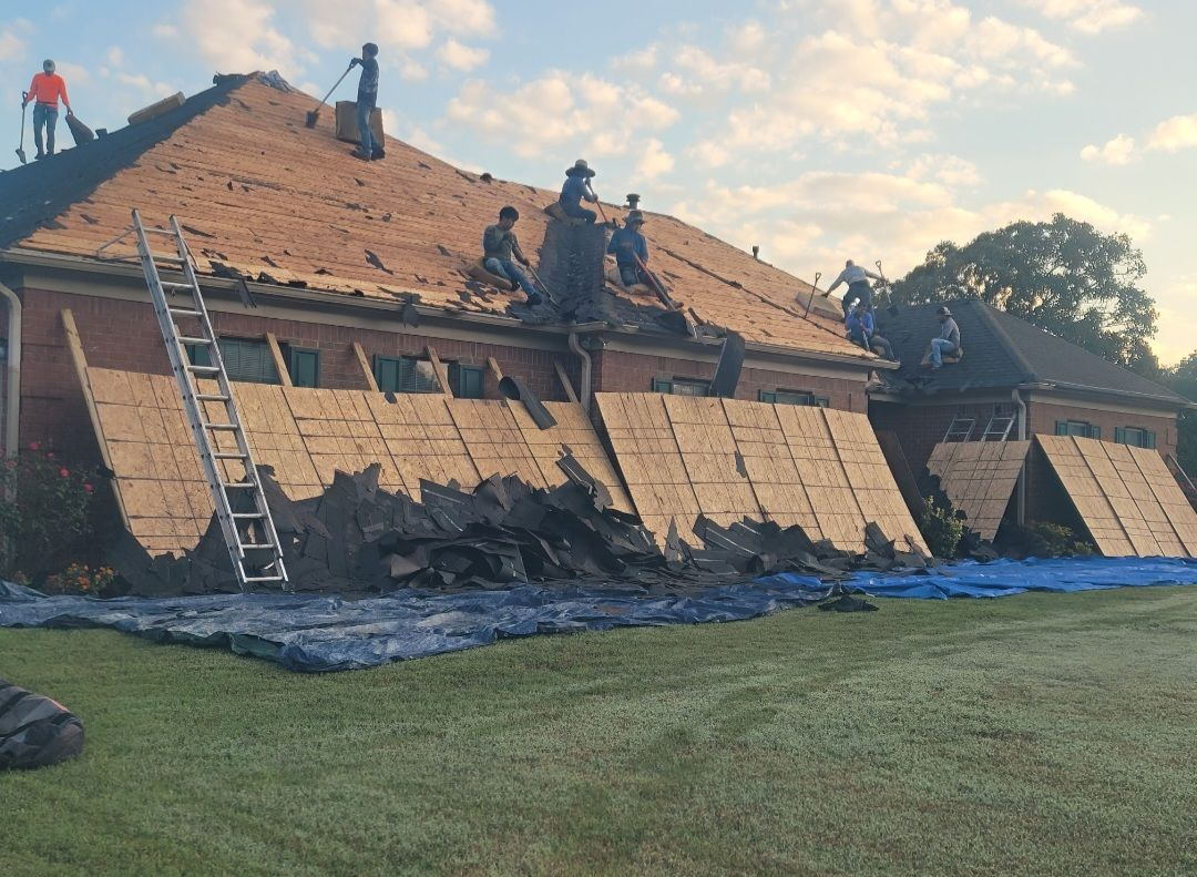 Tan house with dark green roof, gray garage doors, and brick accents. Two people work on a ladder.