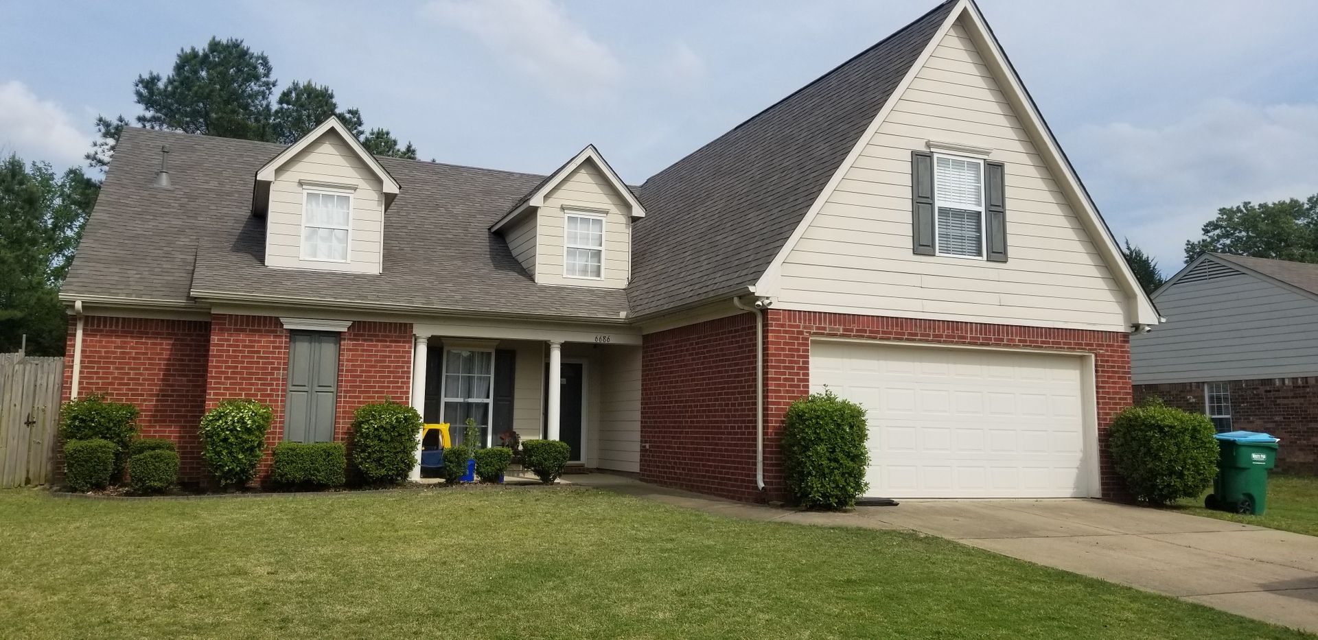 Residential house with red brick facade, white garage door, and green lawn.
