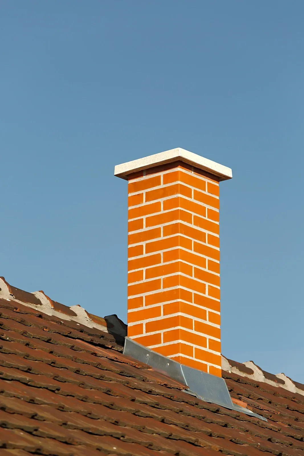 Brick chimney on a tiled roof against a blue sky.