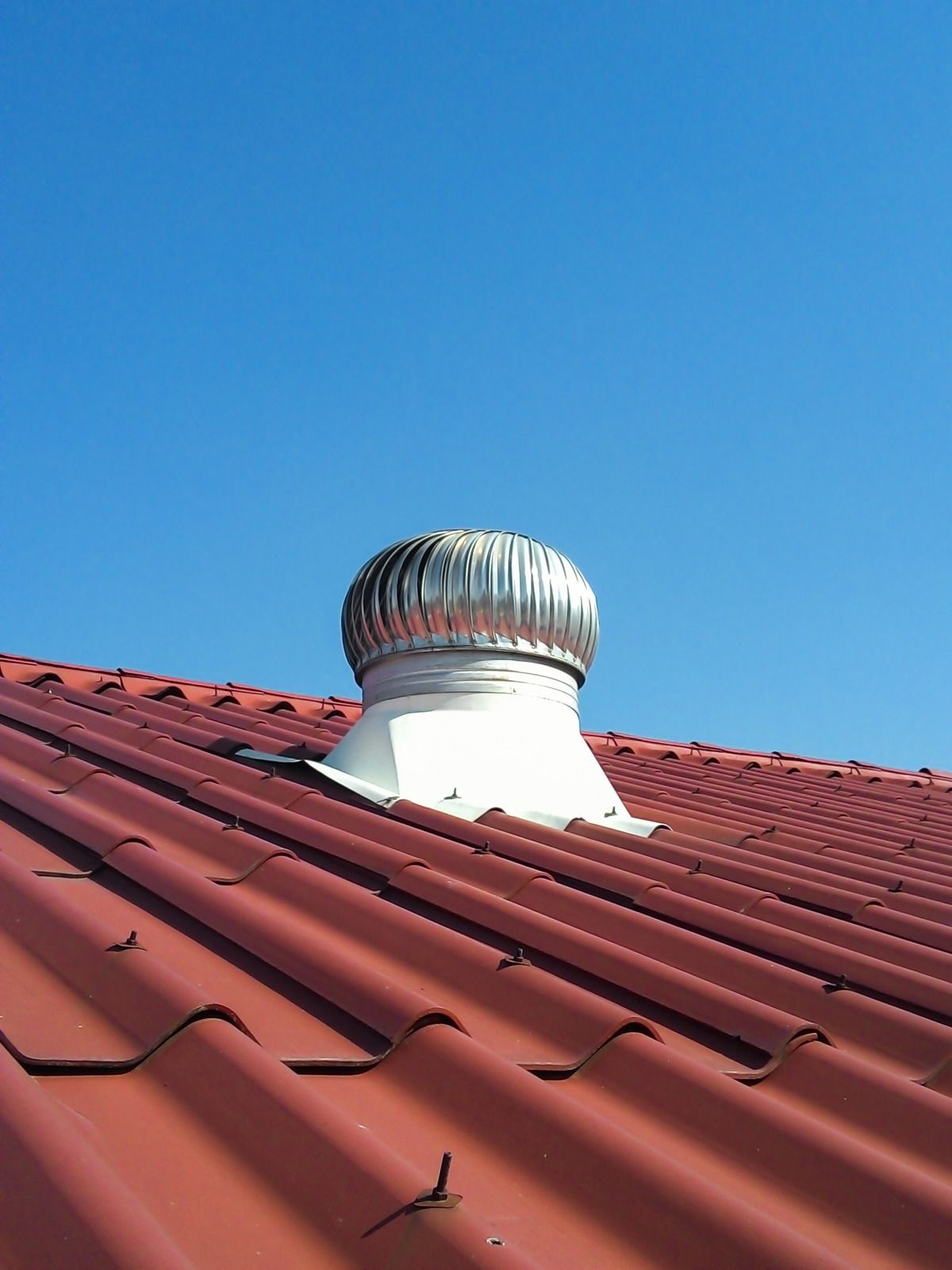 Red roof with a silver, spinning turbine vent against a clear, blue sky.