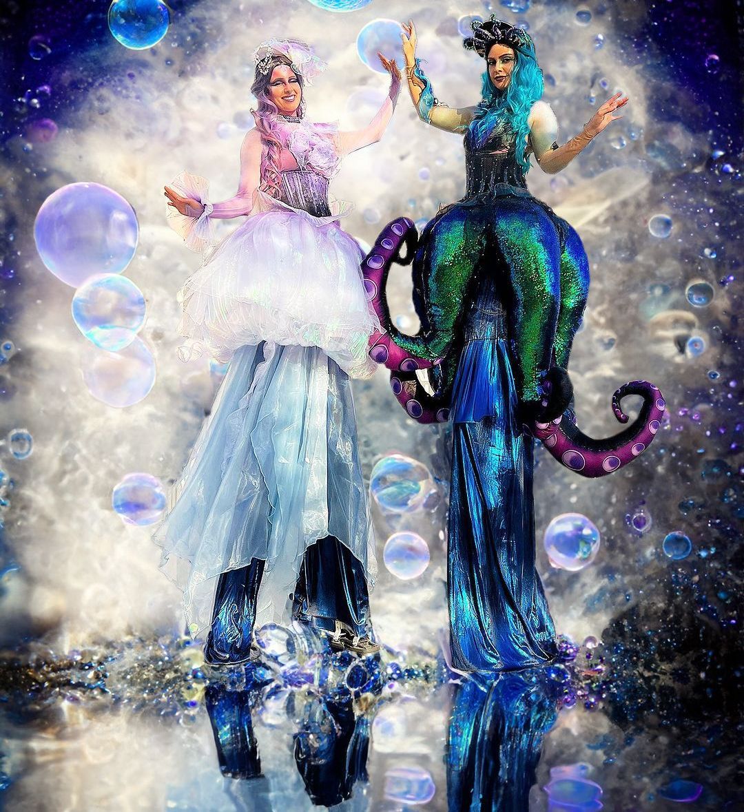 Two women in costumes standing on stilts with bubbles in the background