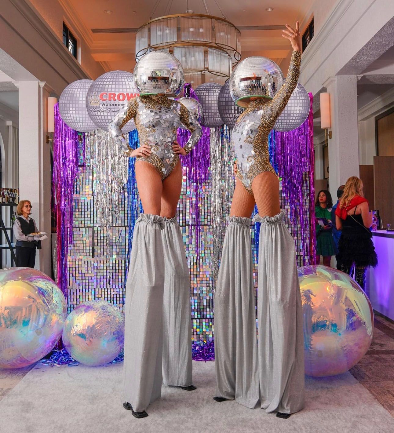 Two women standing on stilts with disco balls on their heads