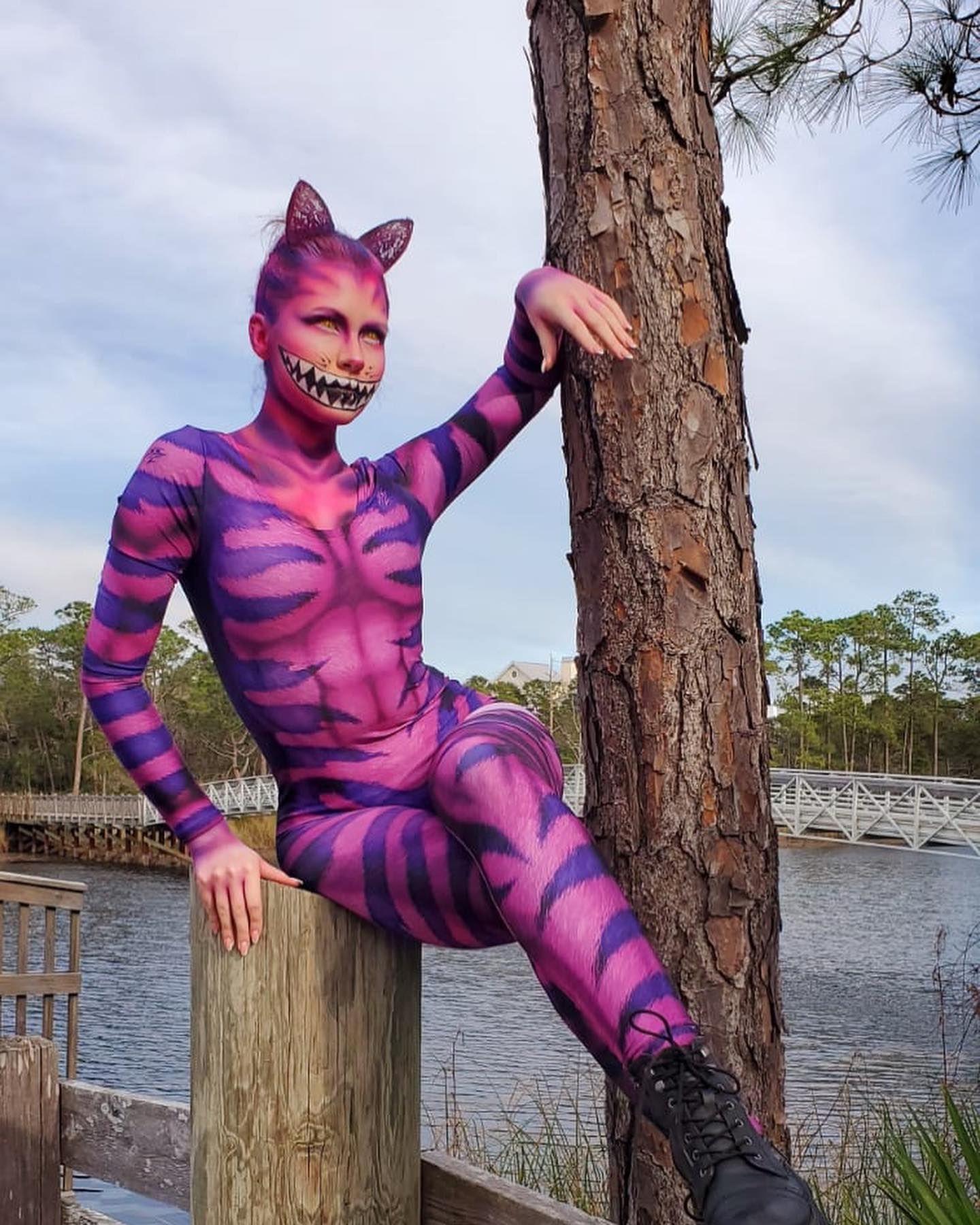 A woman in a cheshire cat costume is leaning against a tree.