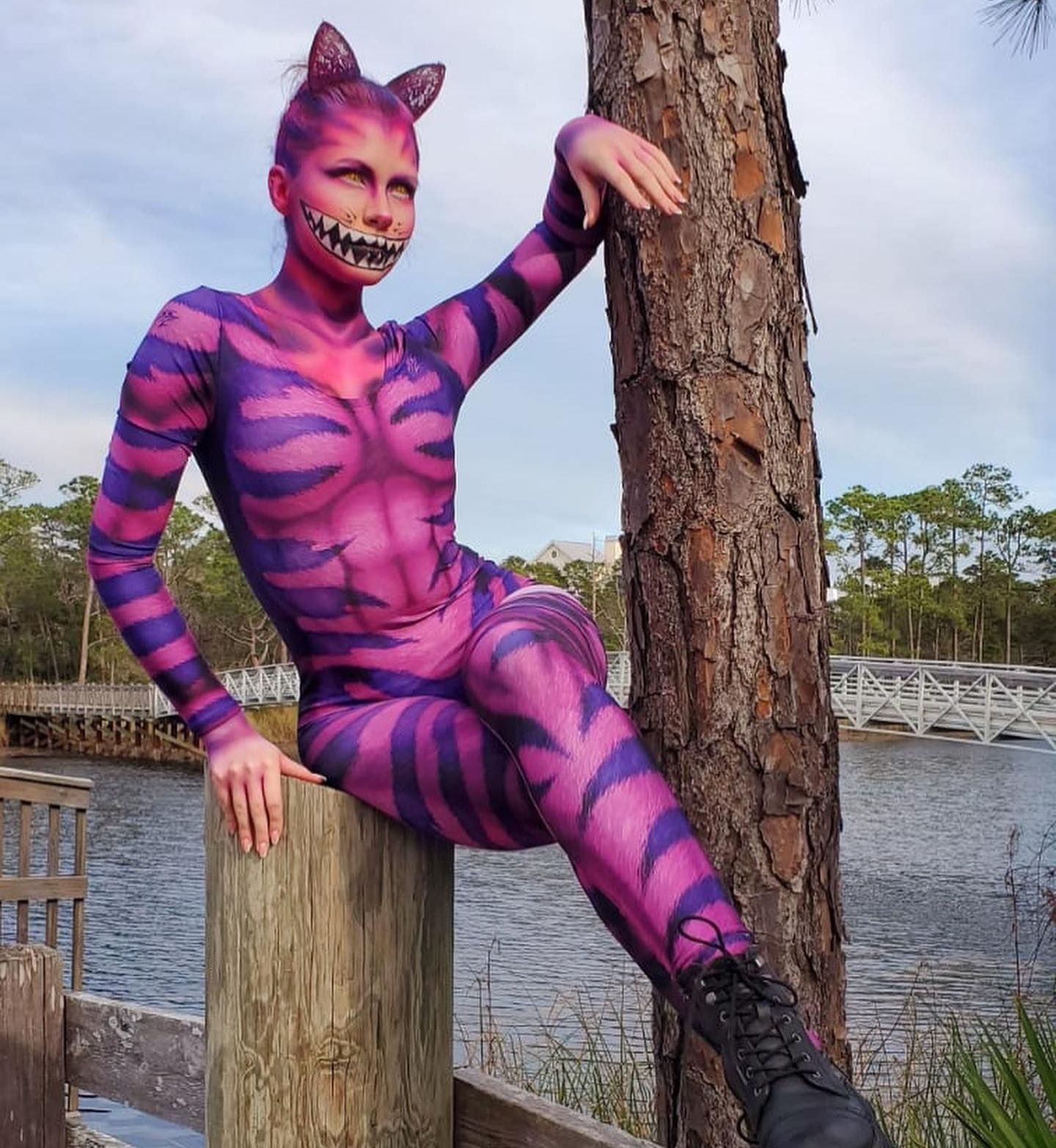 A woman in a cheshire cat costume is sitting on a wooden post