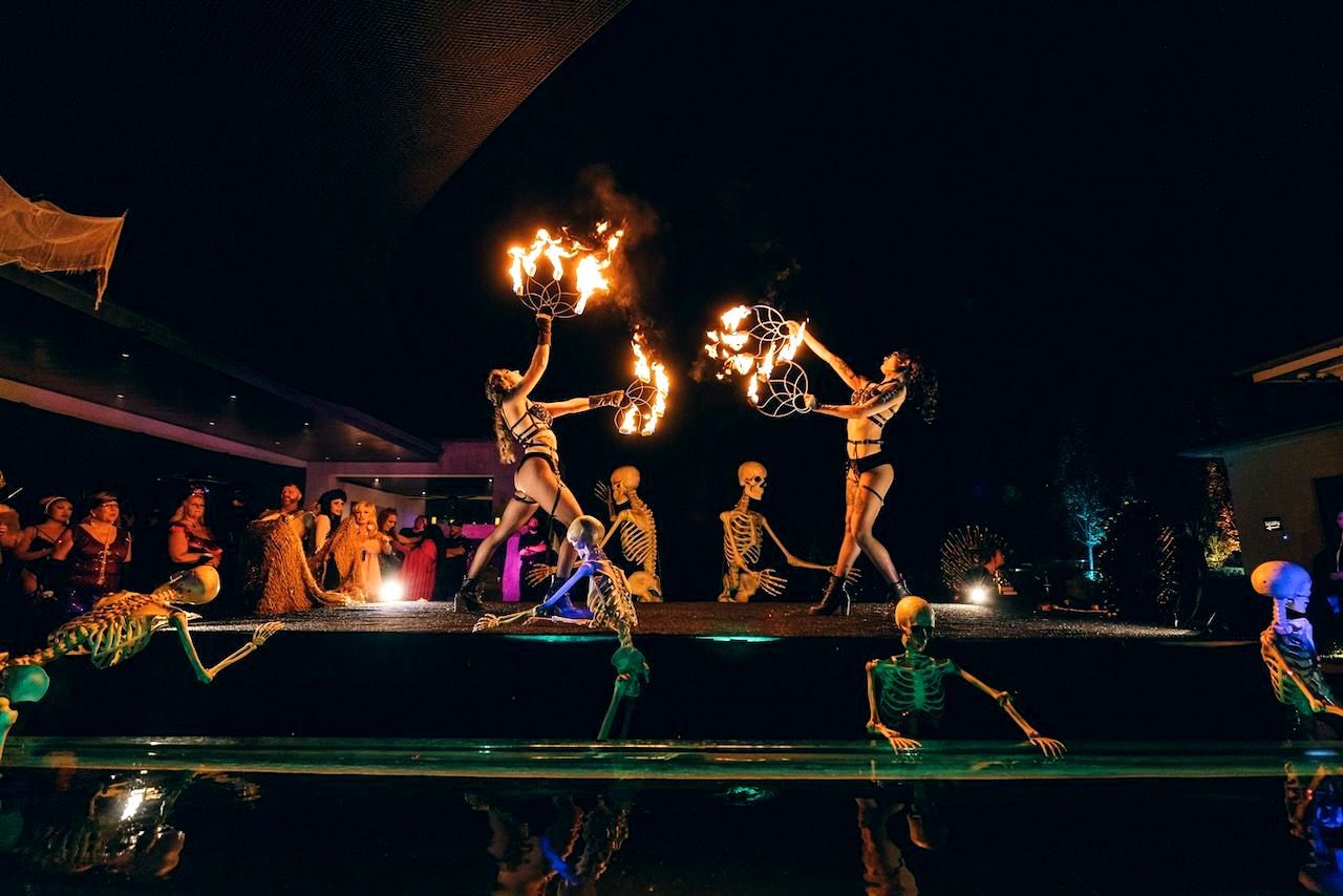 A group of woman are performing a fire show with skeletons on stage.