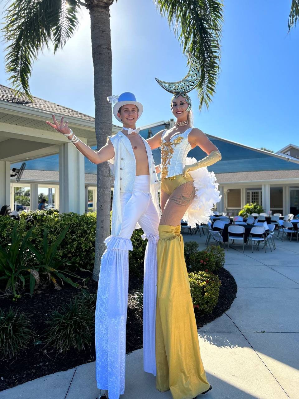 A man and a woman are standing on stilts in front of a building.