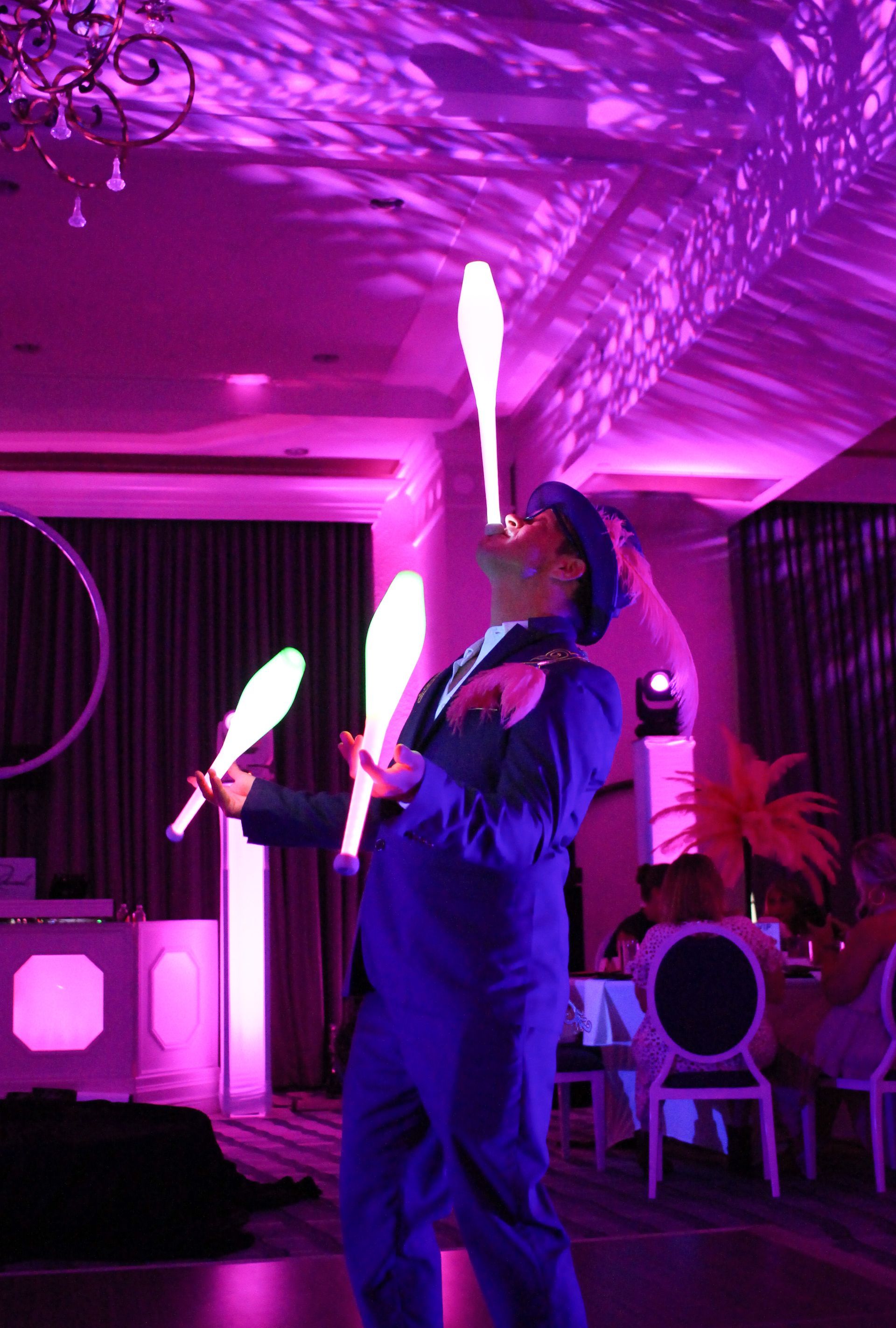 A man in a top hat is juggling clubs in a dark room.