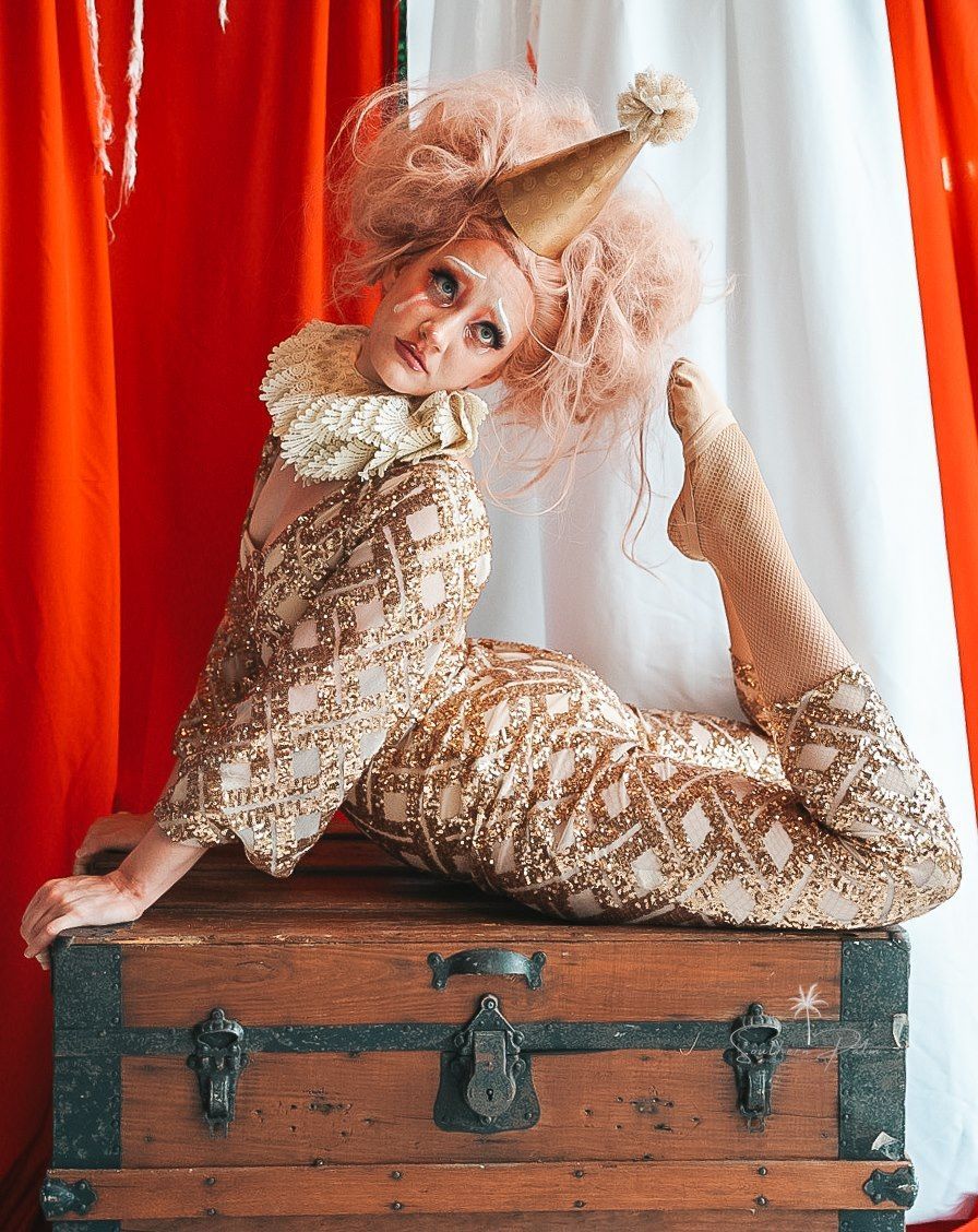a woman in a clown costume is laying on top of a wooden chest